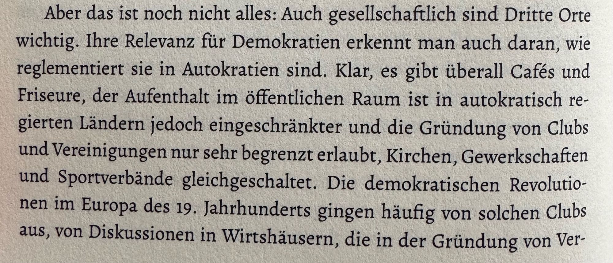 Man sieht ein Foto einer Buchseite mit folgendem Textausschnitt:
„Aber das ist noch nicht alles: Auch gesellschaftlich sind Dritte Orte wichtig. Ihre Relevanz für Demokratien erkennt man auch daran, wie reglementiert sie in Autokratien sind. Klar, es gibt überall Cafés und Friseure, der Aufenthalt im öffentlichen Raum ist in autokratisch regierten Ländern jedoch eingeschränkter und die Gründung von Clubs und Vereinigungen nur sehr begrenzt erlaubt, Kirchen, Gewerkschaften und Sportverbände gleichgeschaltet. Die demokratischen Revolutionen im Europa des 19. Jahrhunderts gingen häufig von solchen Clubs aus, von Diskussionen in Wirtshäusern, die in der Gründung von Ver-“