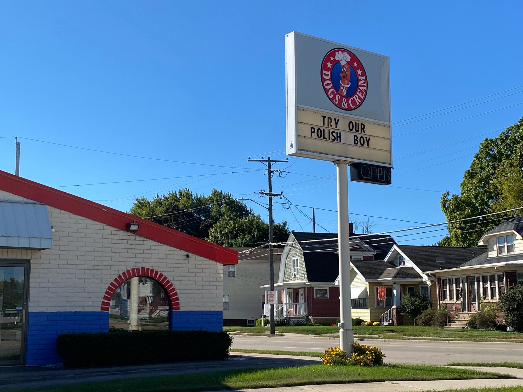 Small, brick restaurant painted red, white, and blue. Large sign on a pole between it and the street. It has movable letters that say TRY OUR POLISH BOY.