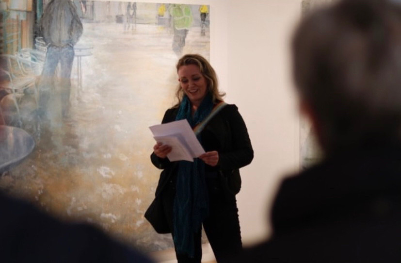 Photo of me, Cristín Leach, standing and reading from an essay I wrote about recent flood paintings by Irish artist Bernadette Kiely in the Lavit Gallery in Cork City. I’m smiling at my own words. 