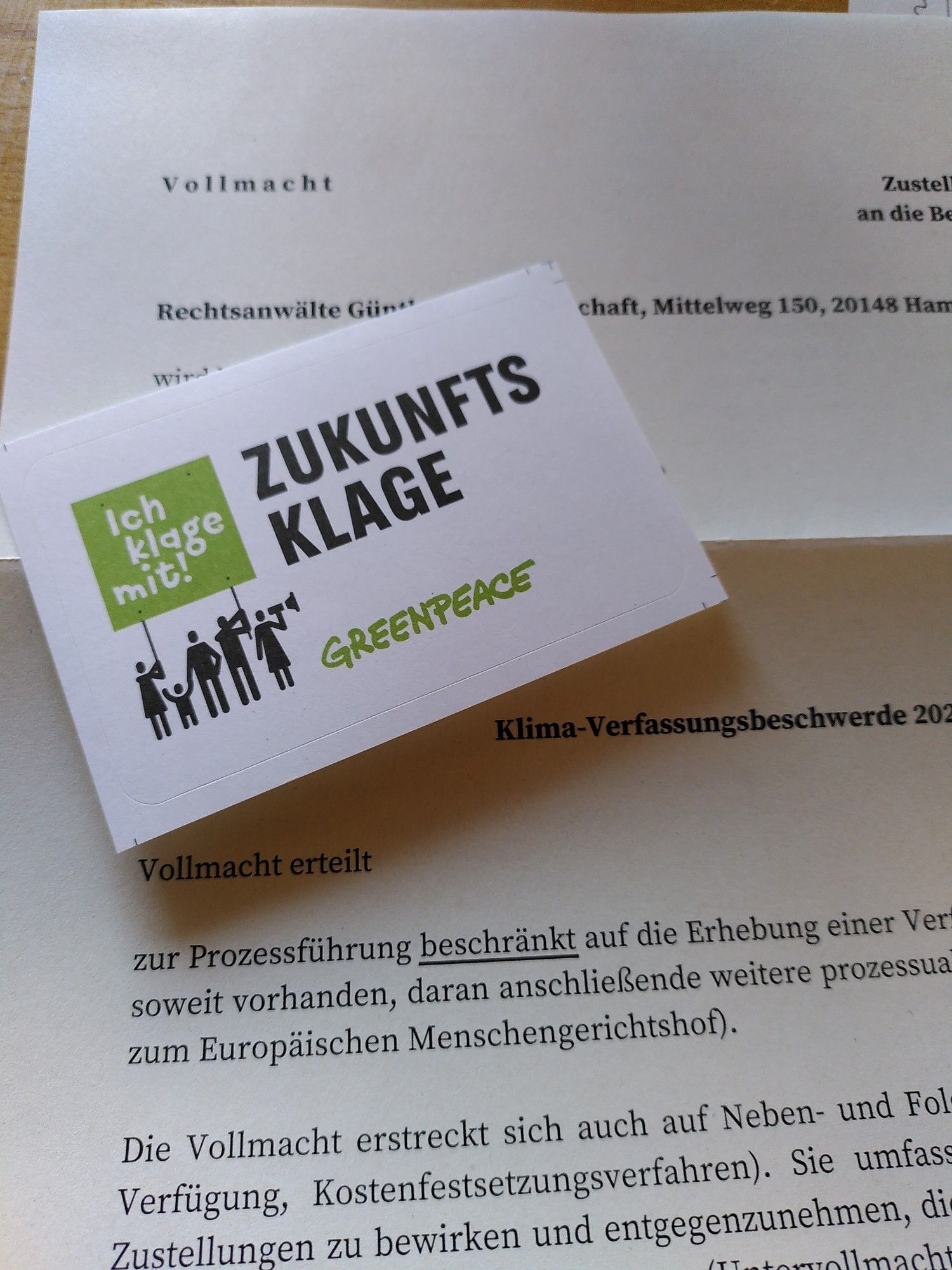 Foto von der Vollmachtsseite, darauf liegt eine Karte von Greenpeace mit Aufschrift "Zukunftsklage"