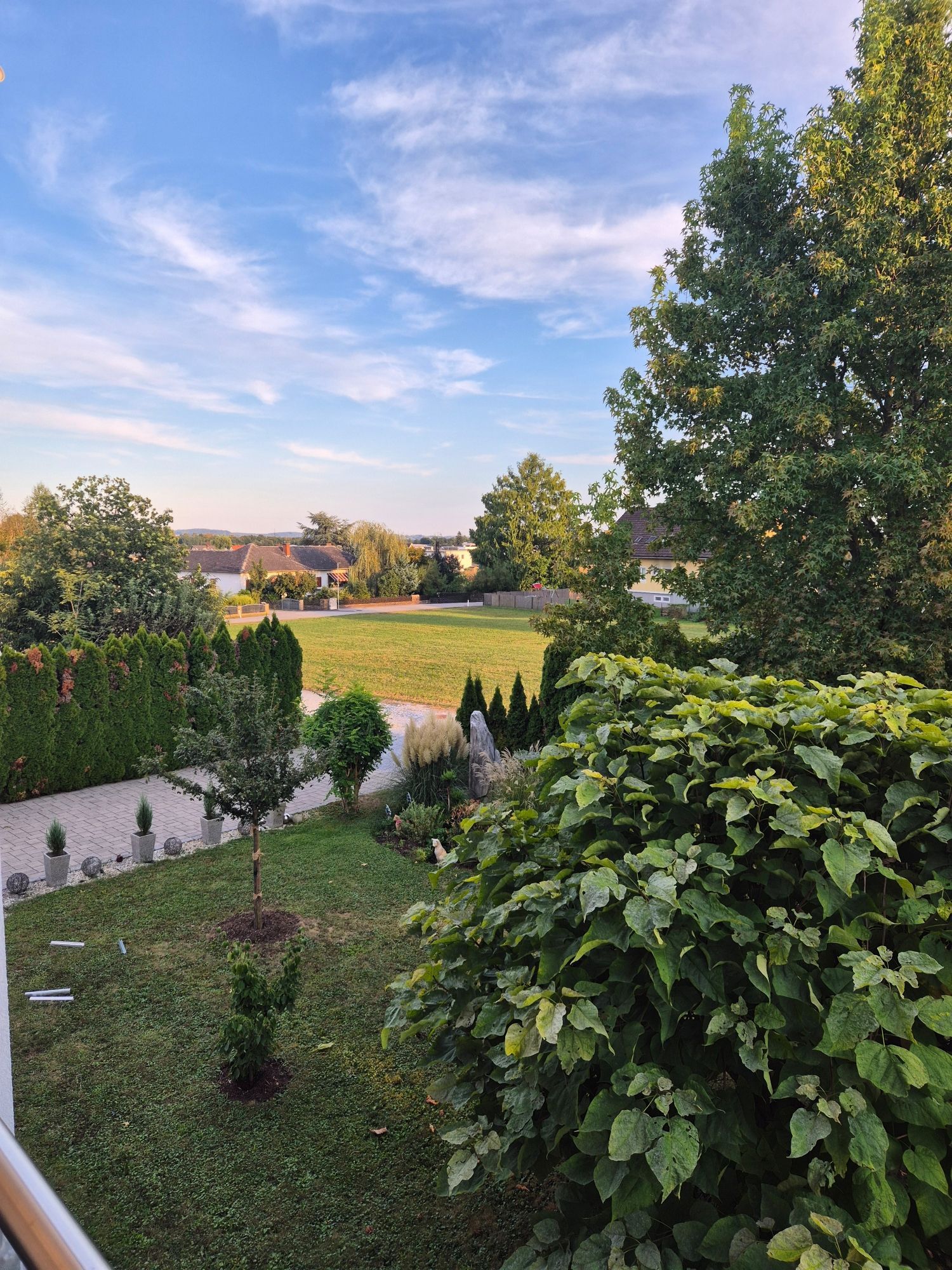 Blick vom ersten Stock auf unserern Garten.  Die Sonne geht bald unter. Der Himmel ist noch blau mit zarten weißen Wolken. Der Wind ist schon recht feucht und kündigt die aufziehende Front an.