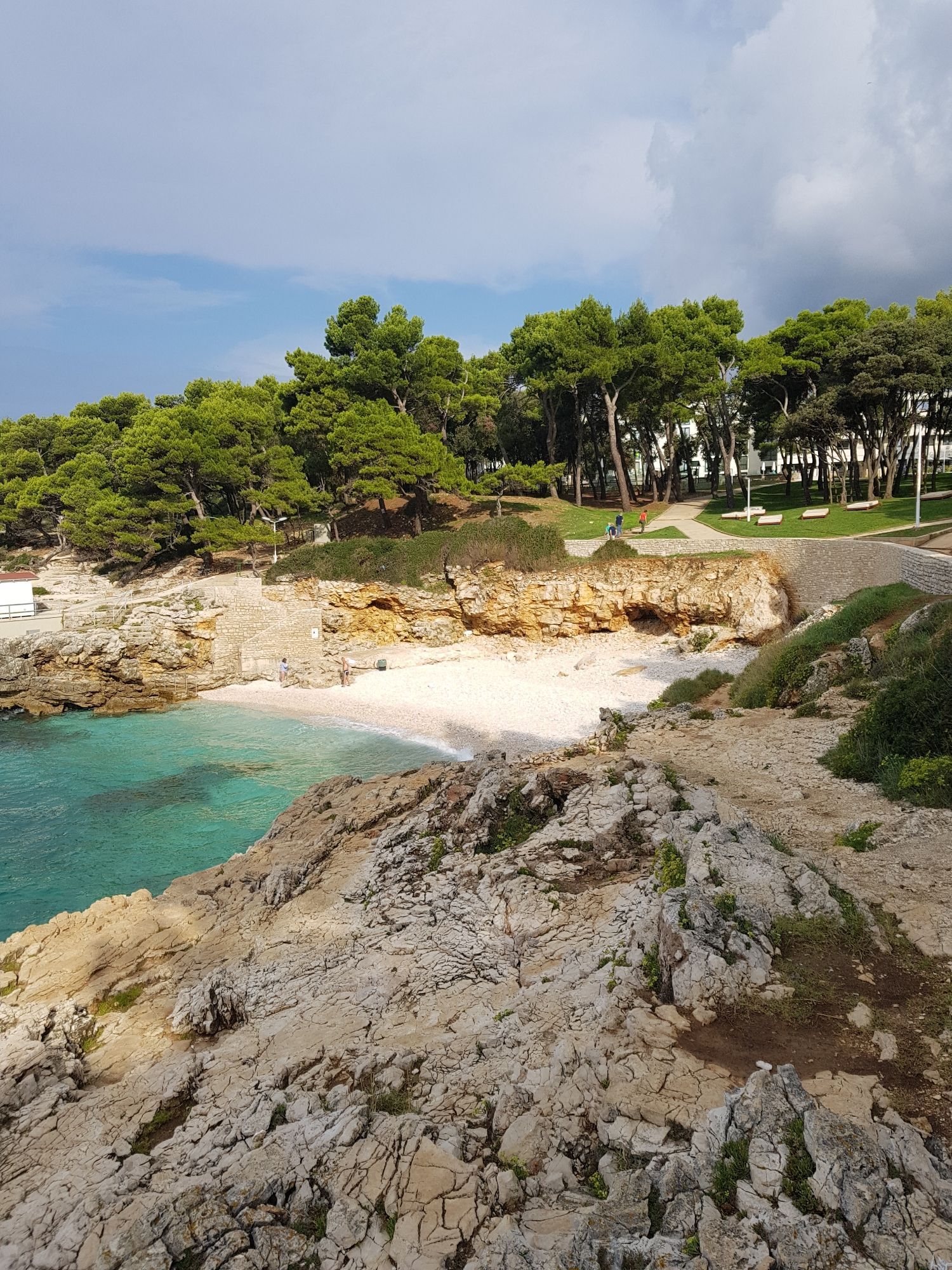 Kleine Bucht in der Nähe von Biran, Kroatien. Schroffe Felsen und etwas feinen Kiesstrand. Das Meer ist strahlend blau, der Himmel leicht bewölkt.