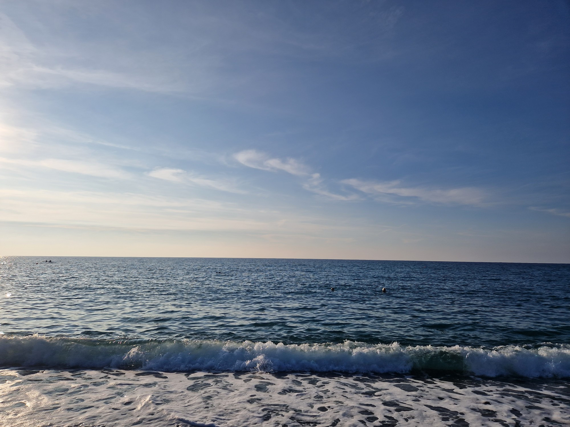 Blauer Himmel über der Ägäis. Kleine Wellen brechen mit weißer Schaumkrone an den Strand. 