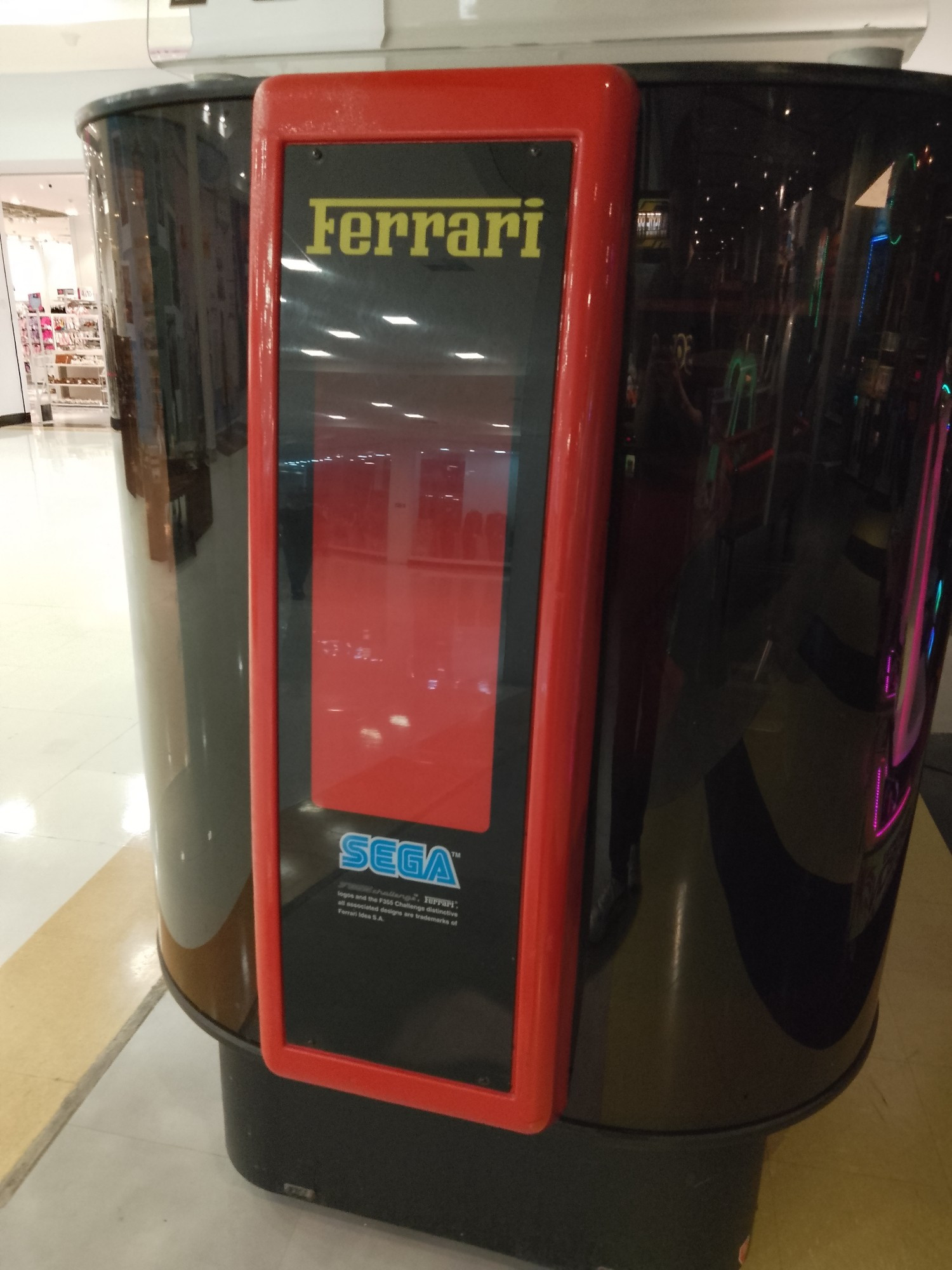 Parte traseira de um fliperama de direção da SEGA, do jogo F355 Challenge. A marca Ferrari e o logo SEGA estão em destaque. O conjunto inteiro do arcade simula uma cabine de piloto.