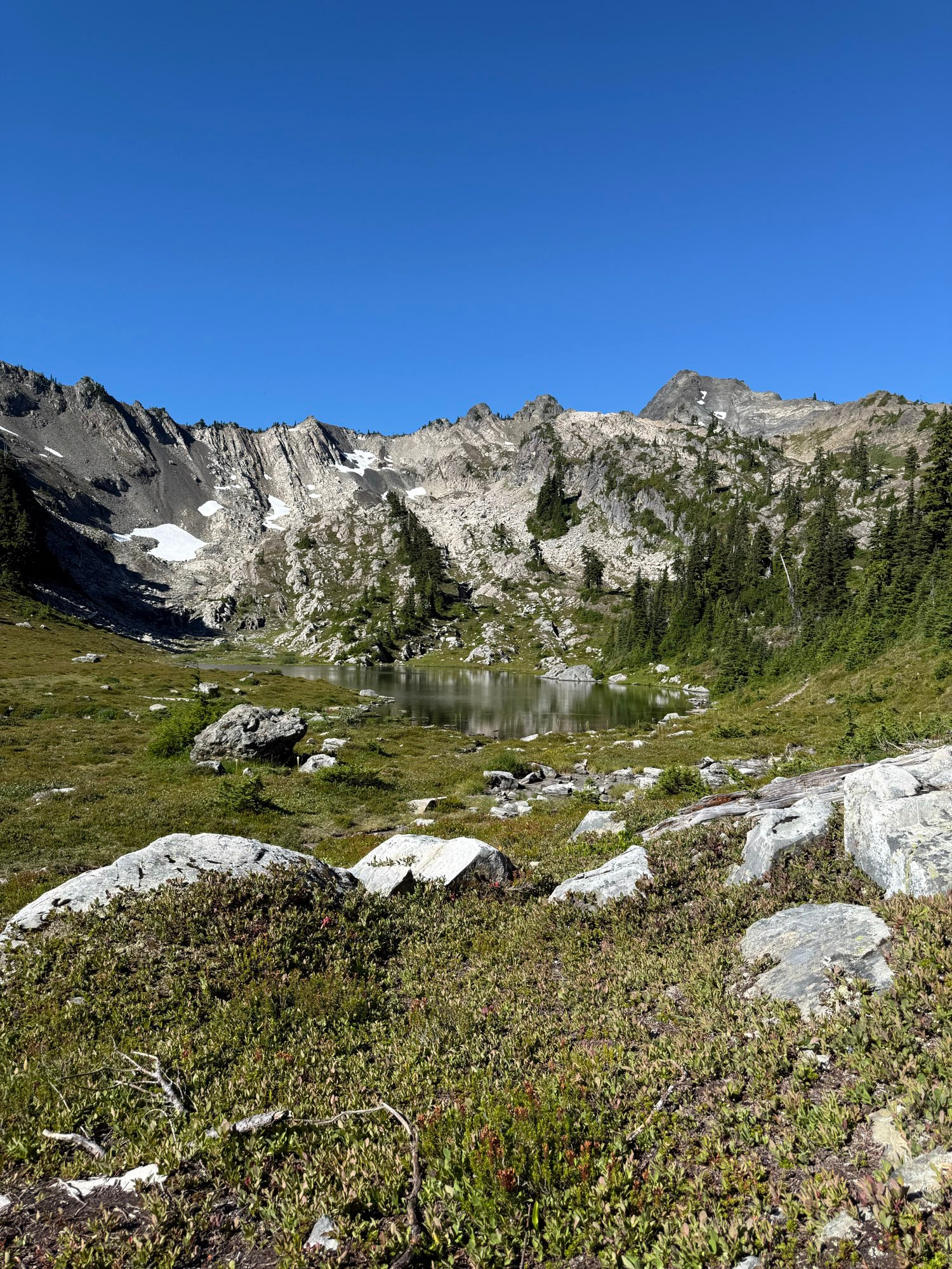 An alpine lake, with majestic rocky mountains rising behind it, dotted with snow. 