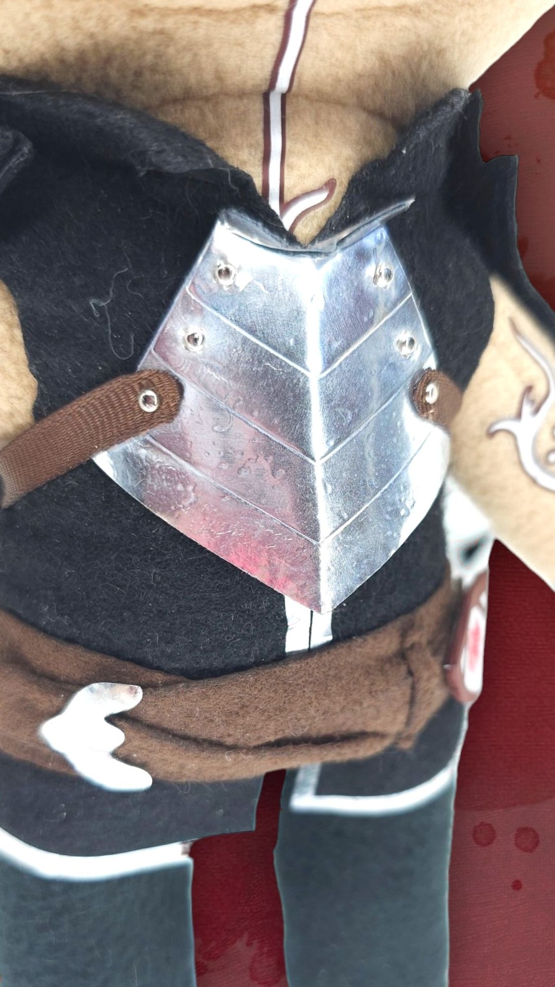 Handmade plush of Fenris from Dragon Age 2, Zoom-in on chest plate to show details. Background is gradient of red/orange/yellow with burn effects.