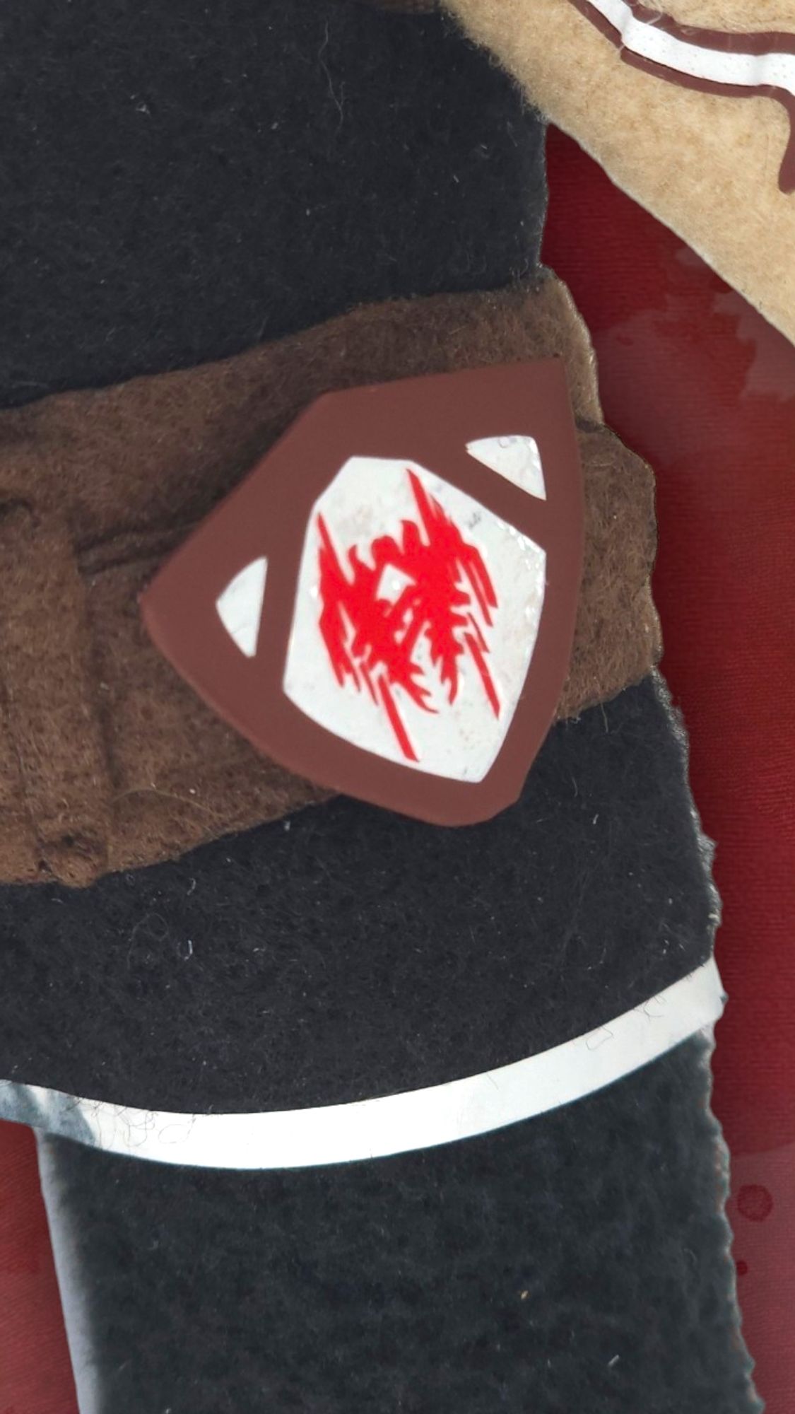 Handmade plush of Fenris from Dragon Age 2, Zoom-in on Amell Family crest on hip to show details. Background is gradient of red/orange/yellow with burn effects.