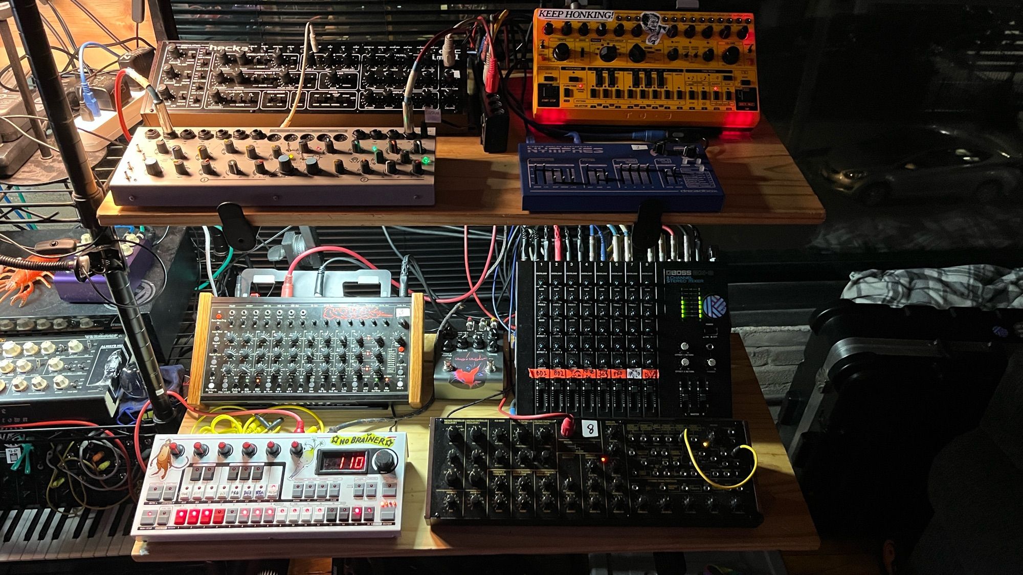 2-tier stand setup with a bunch of music gear - sequencer, synths, drum machine, effects, and a mixer