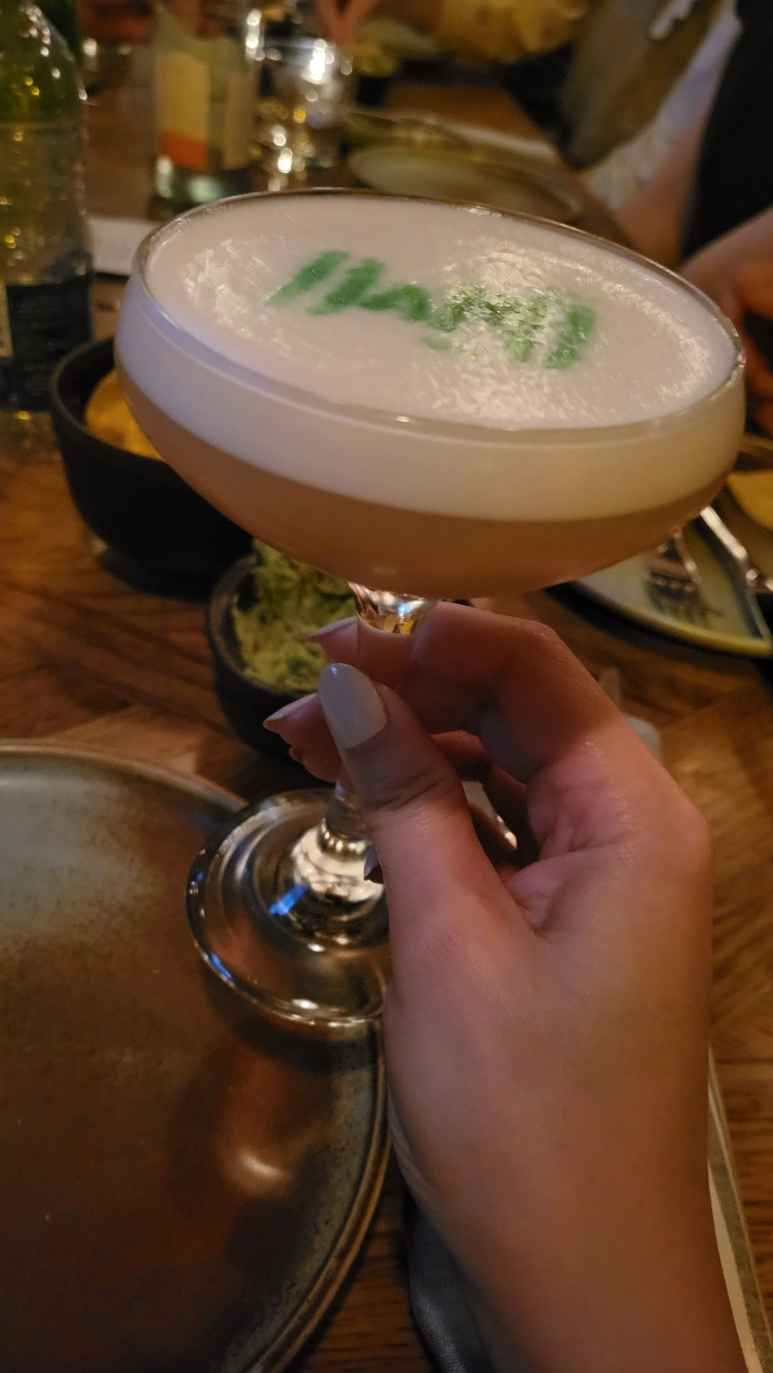 holding a pale yellow cocktail with foam on top that had guava in it