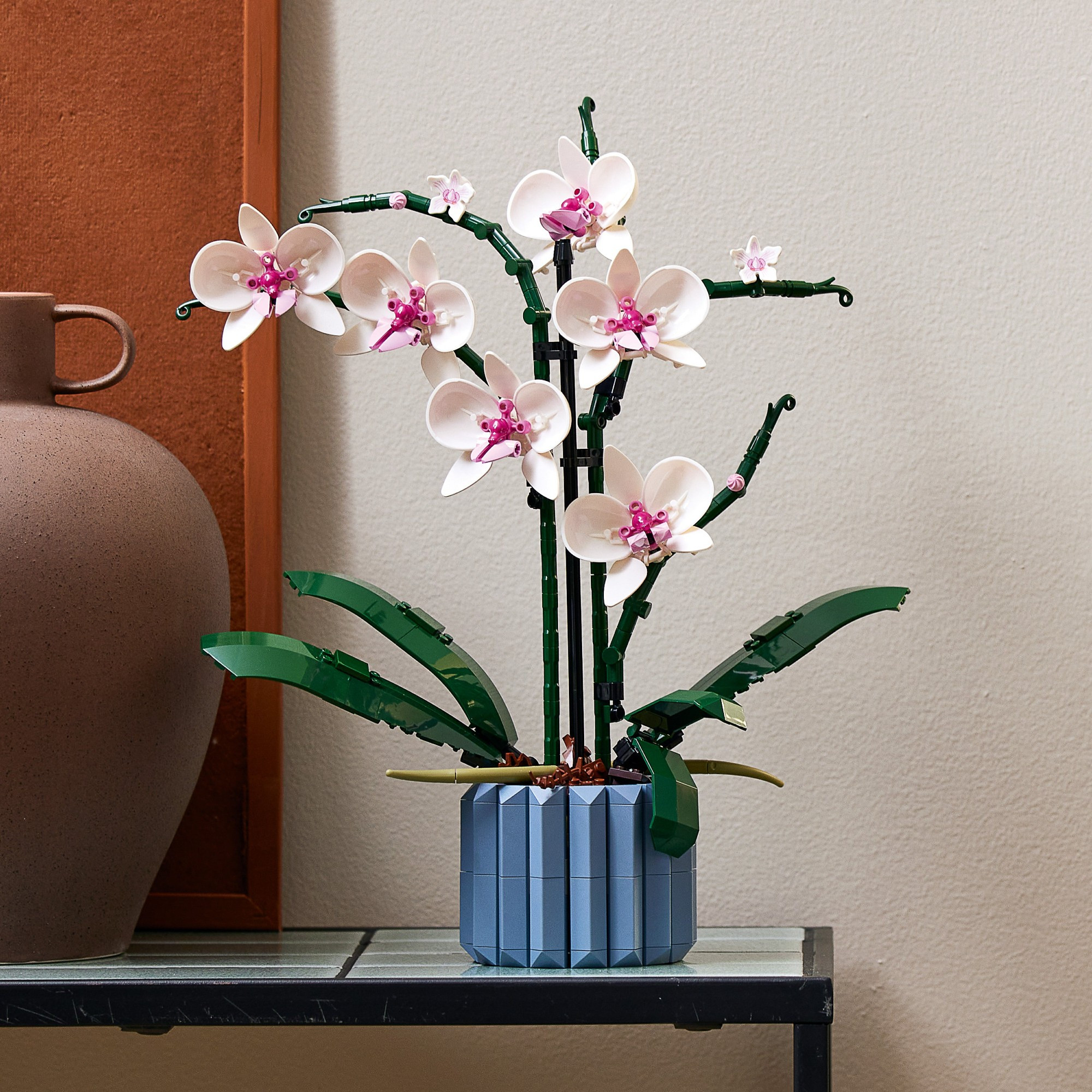 Pink Lego orchid kit sitting on a side table in front of a beige wall