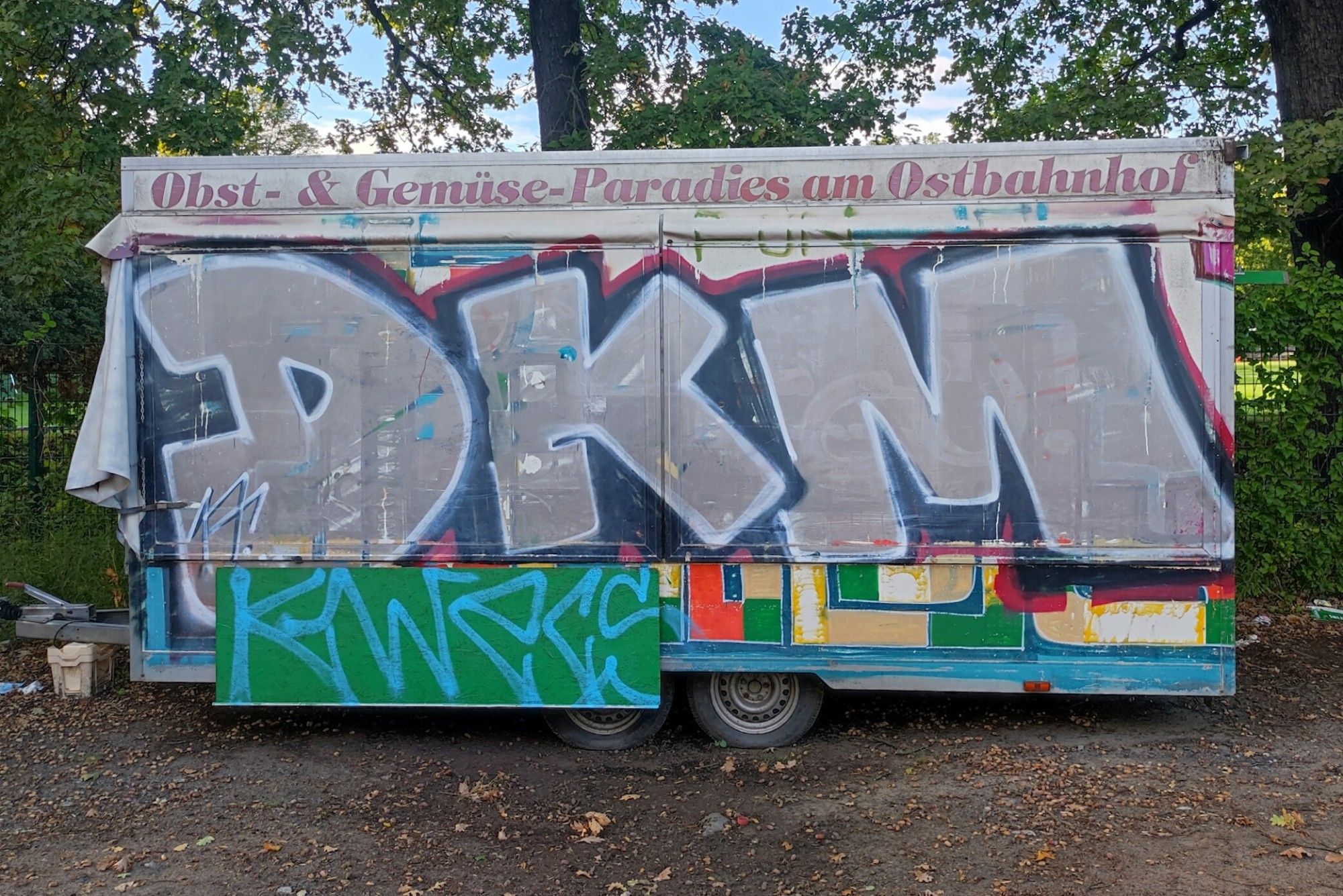 Mit Graffiti überzogener Verkaufsanhänger mit der Aufschrift "Obst- & Gemüse-Paradies am Ostbahnhof"