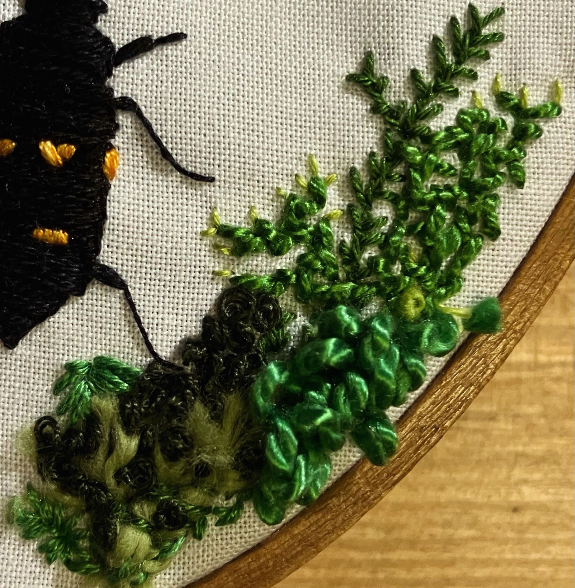 A close up of textured embroidery in many shades of green. It might look like moss.