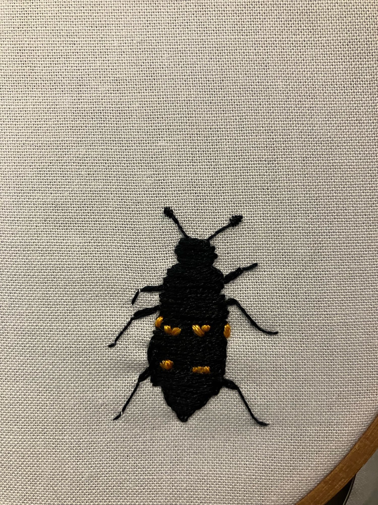 An embroidered burying beetle, black with orange spots.