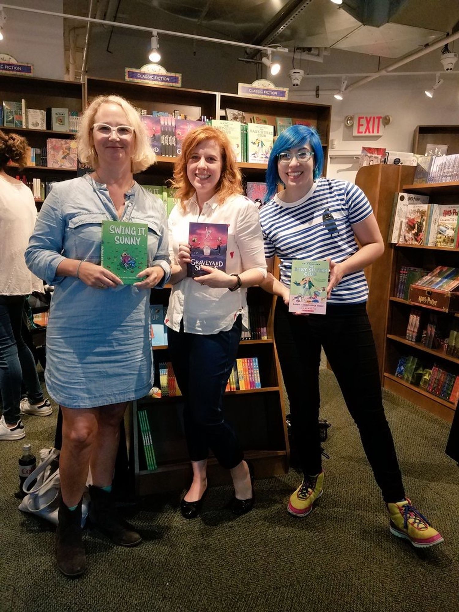 Photo from a book launch event in 2017. Three authors hold up their books. From left: Jenni Holm with Swing It, Sunny; Laura Terry with Graveyard Shakes; Gale Galligan with Dawn and the Impossible Three.