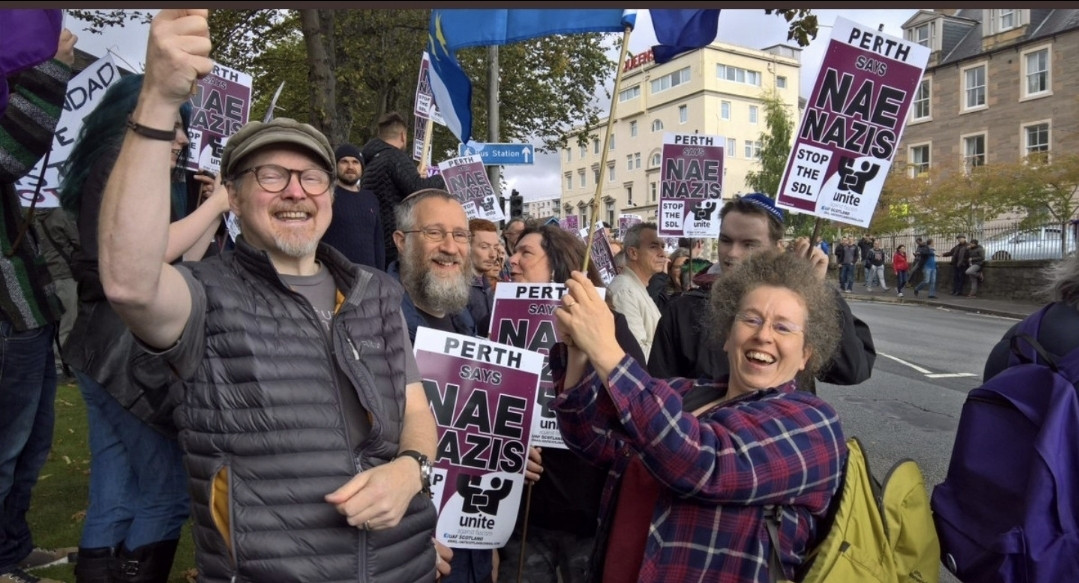 A rally full of cheerful people holding nae nazis placards