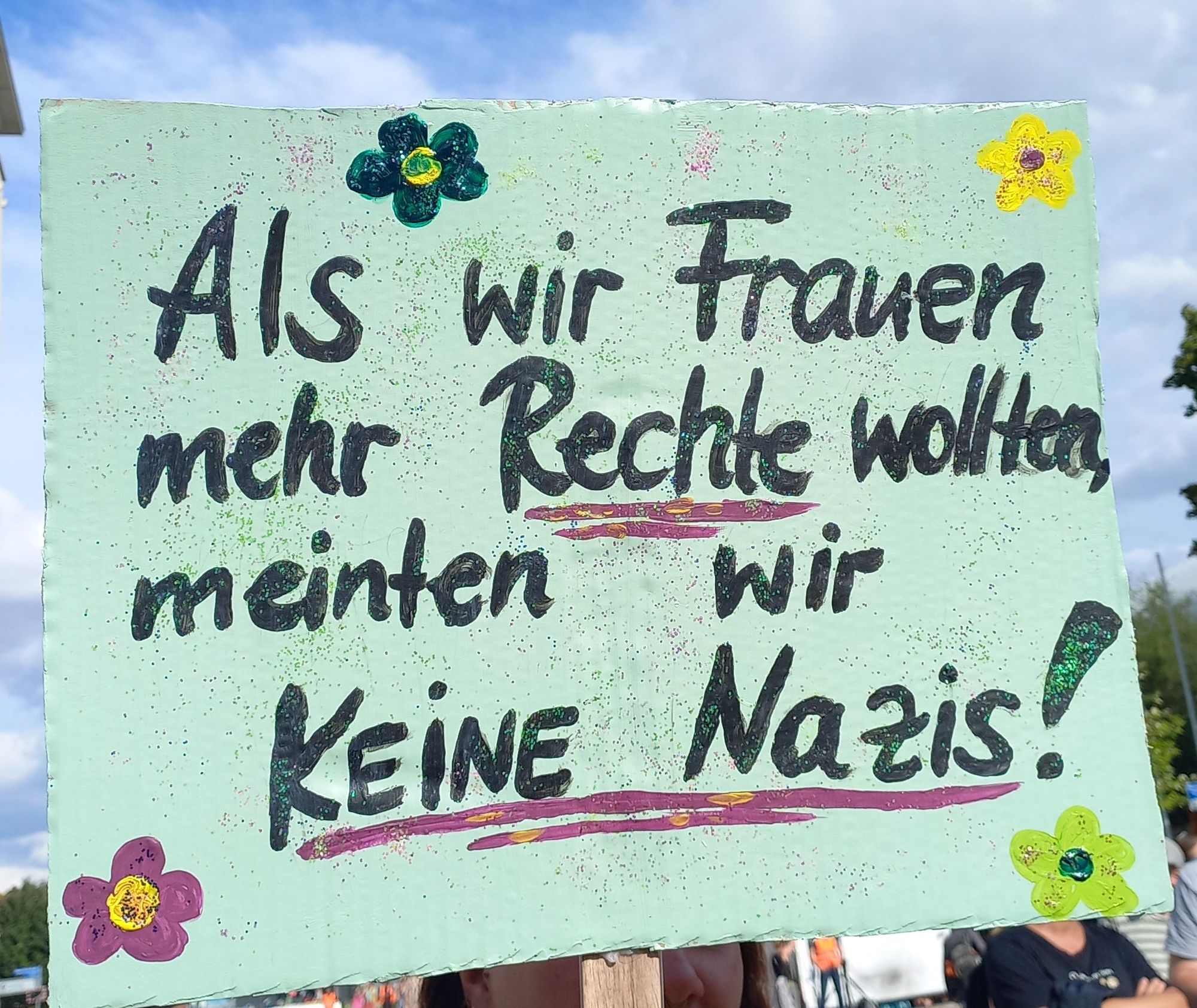 Demo Transpi mit der Aufschrift "Als wir Frauen mehr Rechte wollten, meinten wir keine Nazis!" Dazu Glitzer und Blümchen