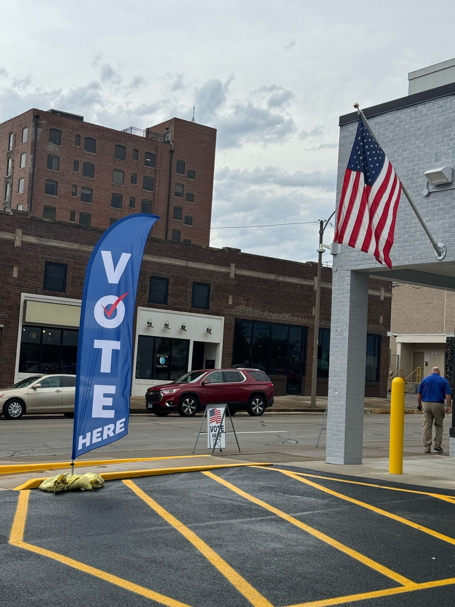 Picture of a city street that features an American flag on one building and two different signs indicating the building is a polling place.