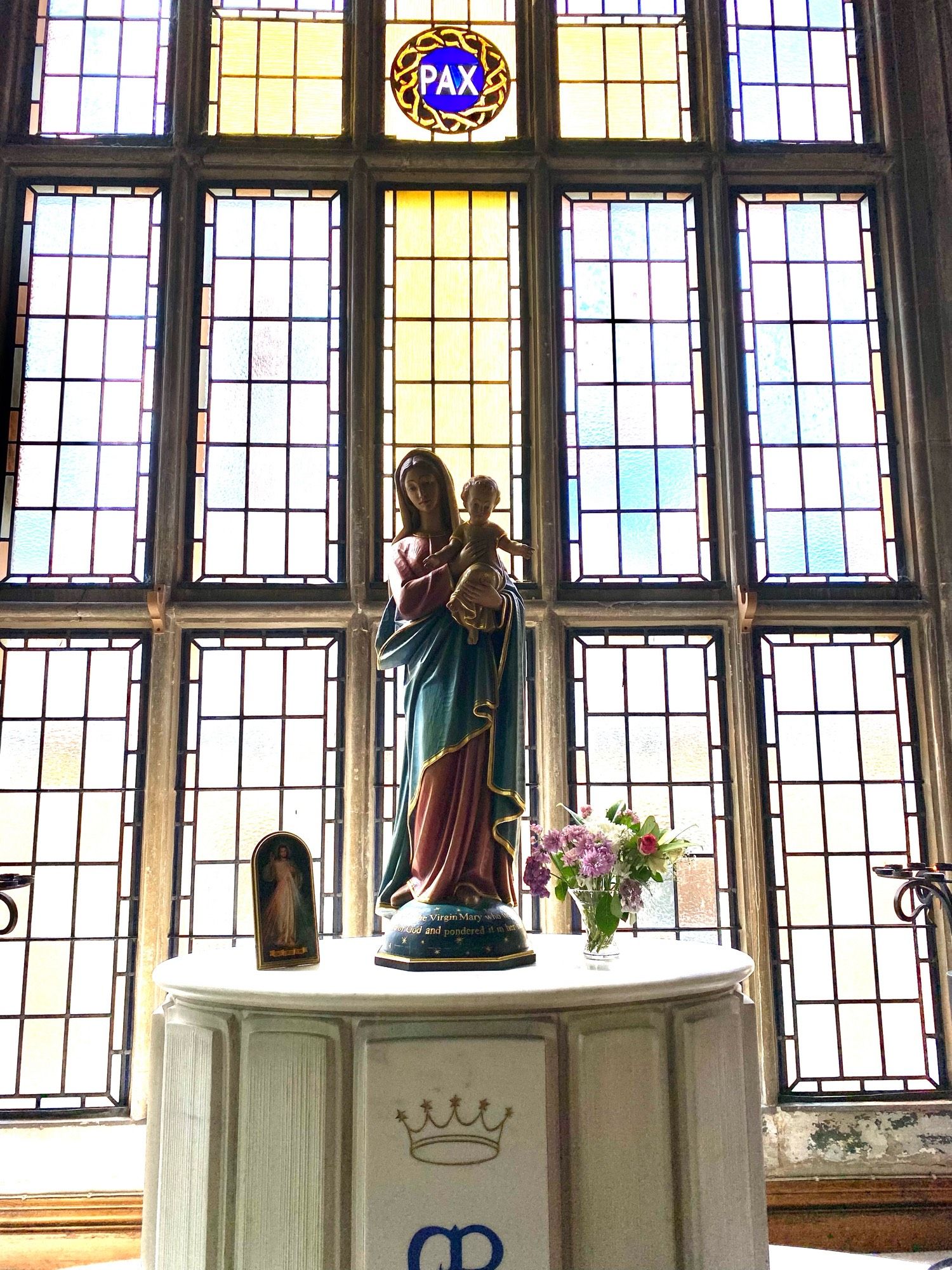 Statue of the Virgin Mary holding baby Jesus in front of tall stain glass windows