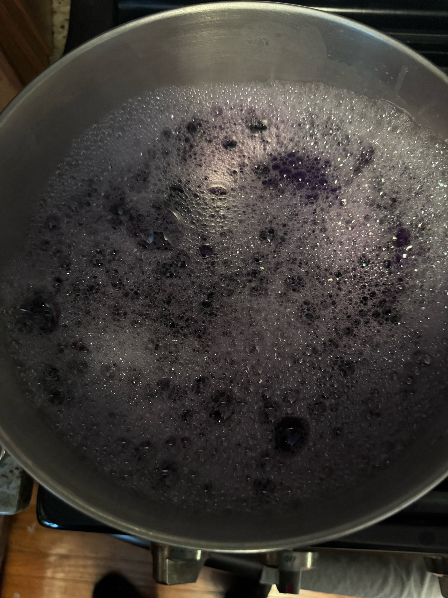 Cotton fabric dyed purple in a bubbly color dye solution in a stainless steel pot on a stove.