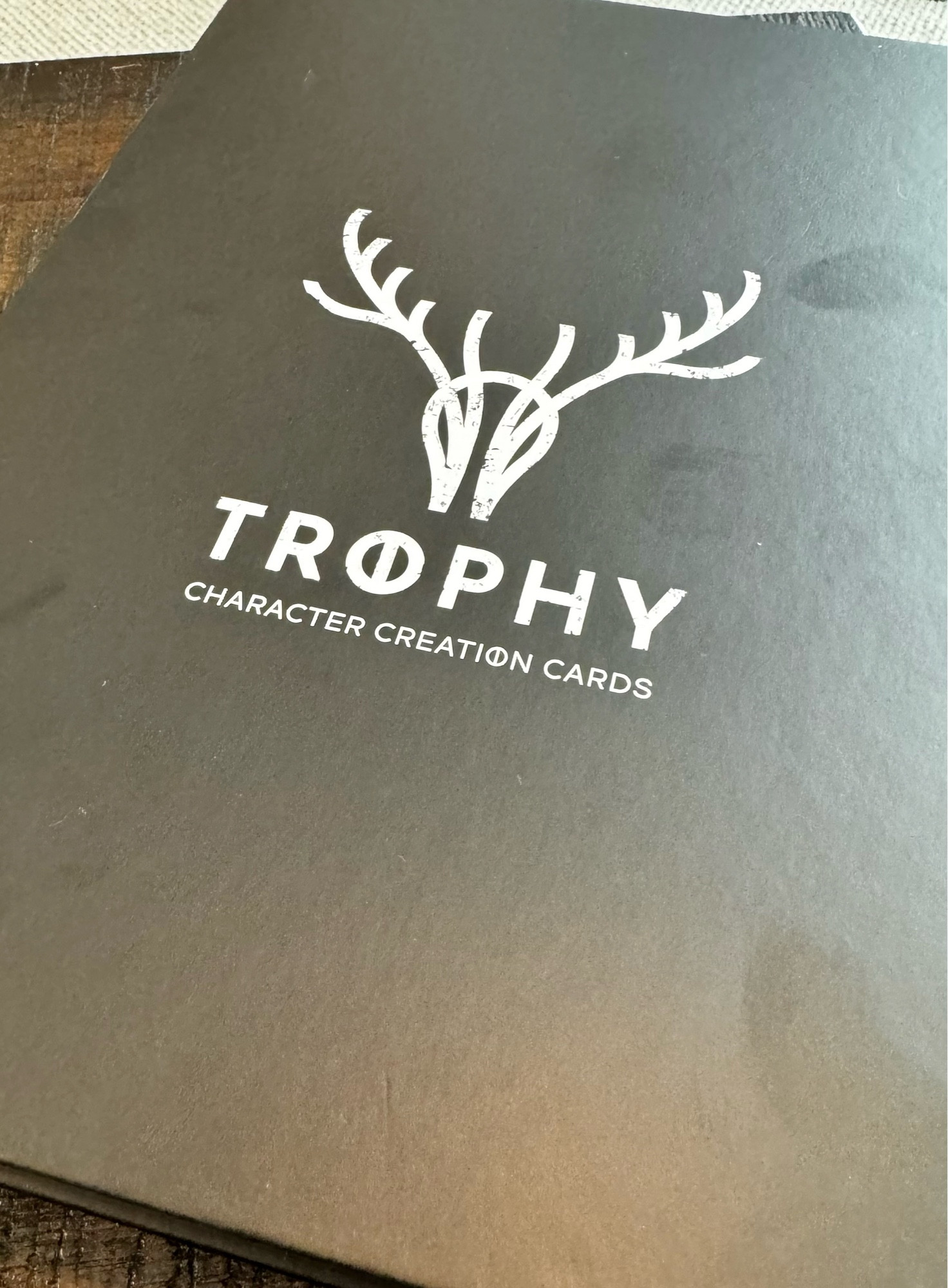 The front of a black box that says “Trophy Character Creation Cards” below a stylized logo of a buck’s head and antlers