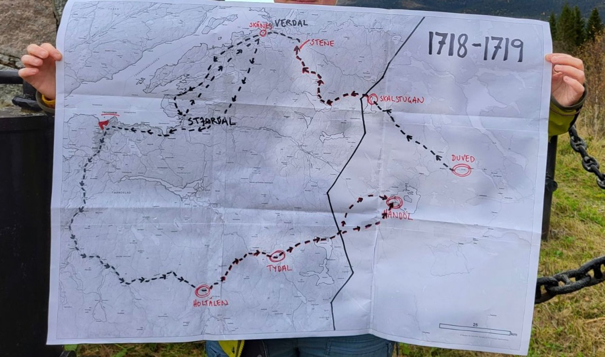 Foto av et svart/hvitt topografisk kart over Trøndelag og Jämtlamd, teipa sammen av ni A4-ark, med stipla linjer og viktige stedsnavn fra Armfelds karoliner-felttog i 1718/-19 tegna på med rød og svart sprittusj