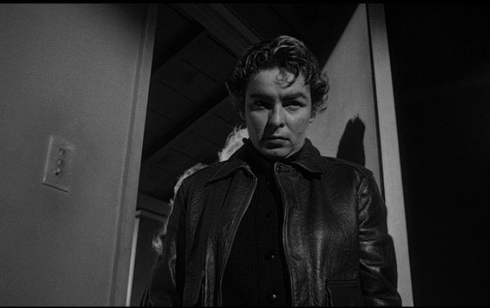 Mercedes McCambridge, butched out in a leather motorcycle jacket and a Fonzie hairdo, enters Janet Leigh's motel room in a screengrab from A Touch of Evil (1958). 