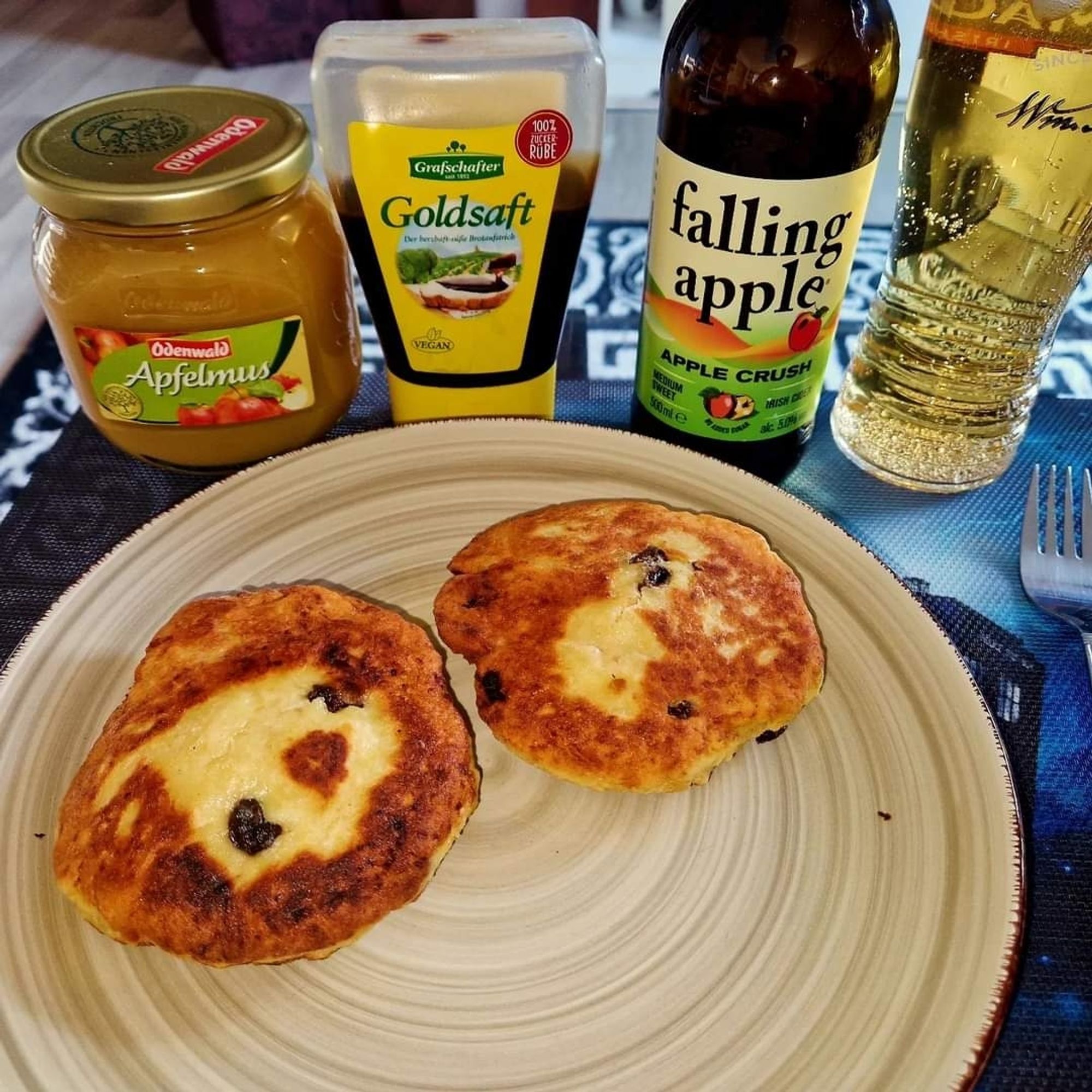 Ein Teller mit 2 Pickert. Dahinter stehen eine Flasche Zuckerrübensirup und ein Glas Apfelmus. Dazu irischer Cider von "Falling Apple"