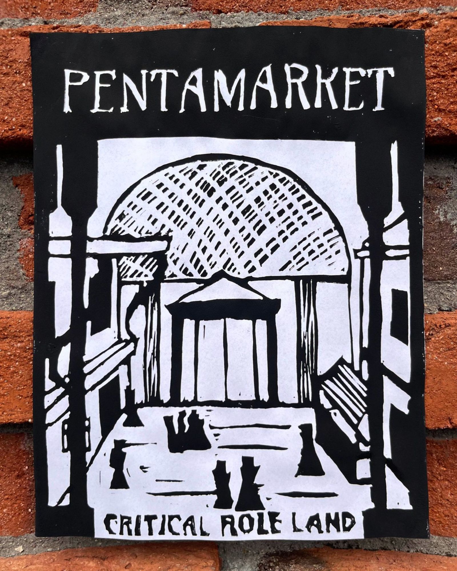 A lino print poster on a brick wall, showing a market district with shops and people walking through it. It's viewed through a colonnade and at the back of it there is a large domed structure.