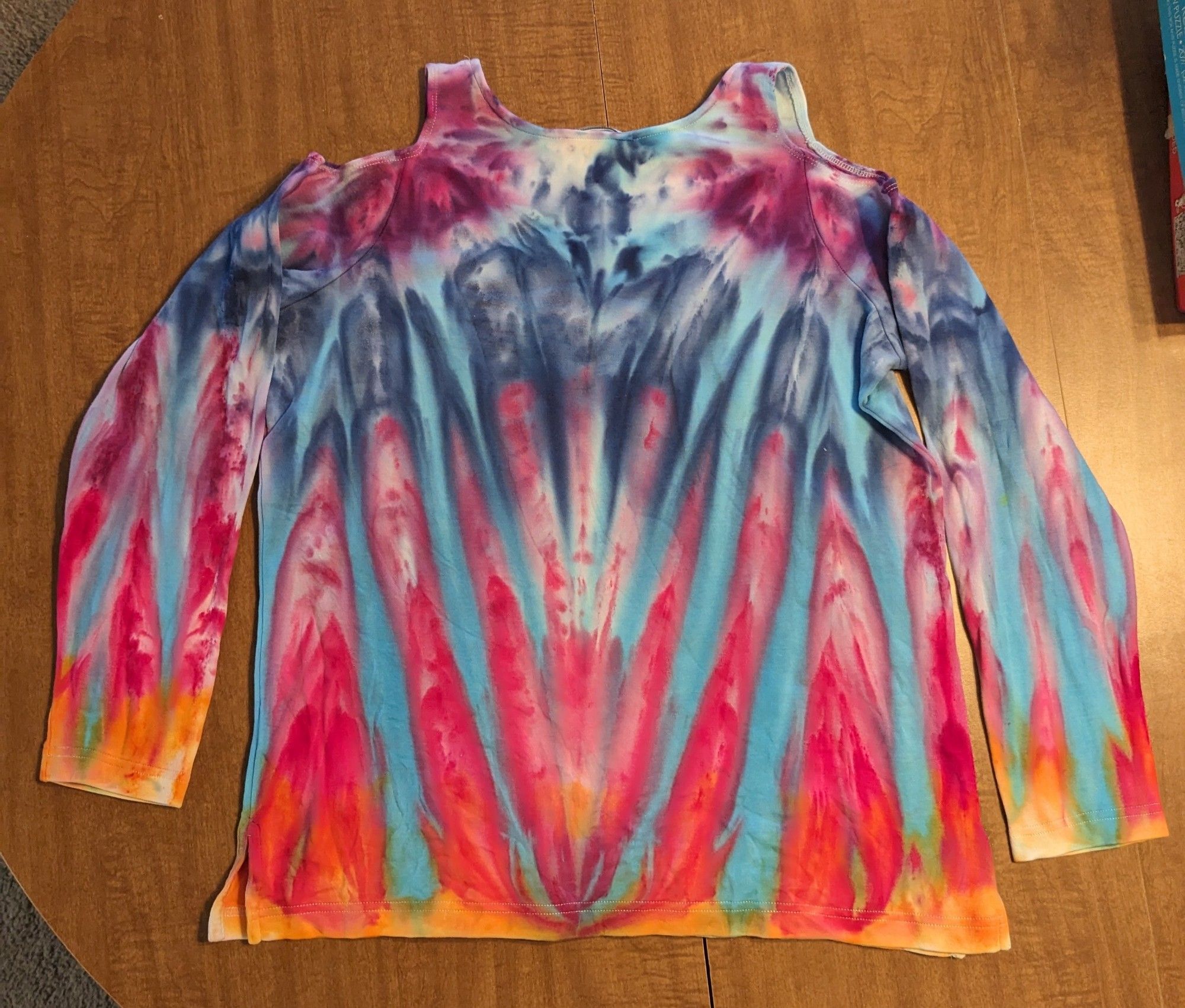 A long sleeve shirt with shoulder cut outs that has been tie dyed with purple, blue, pink, and orange.