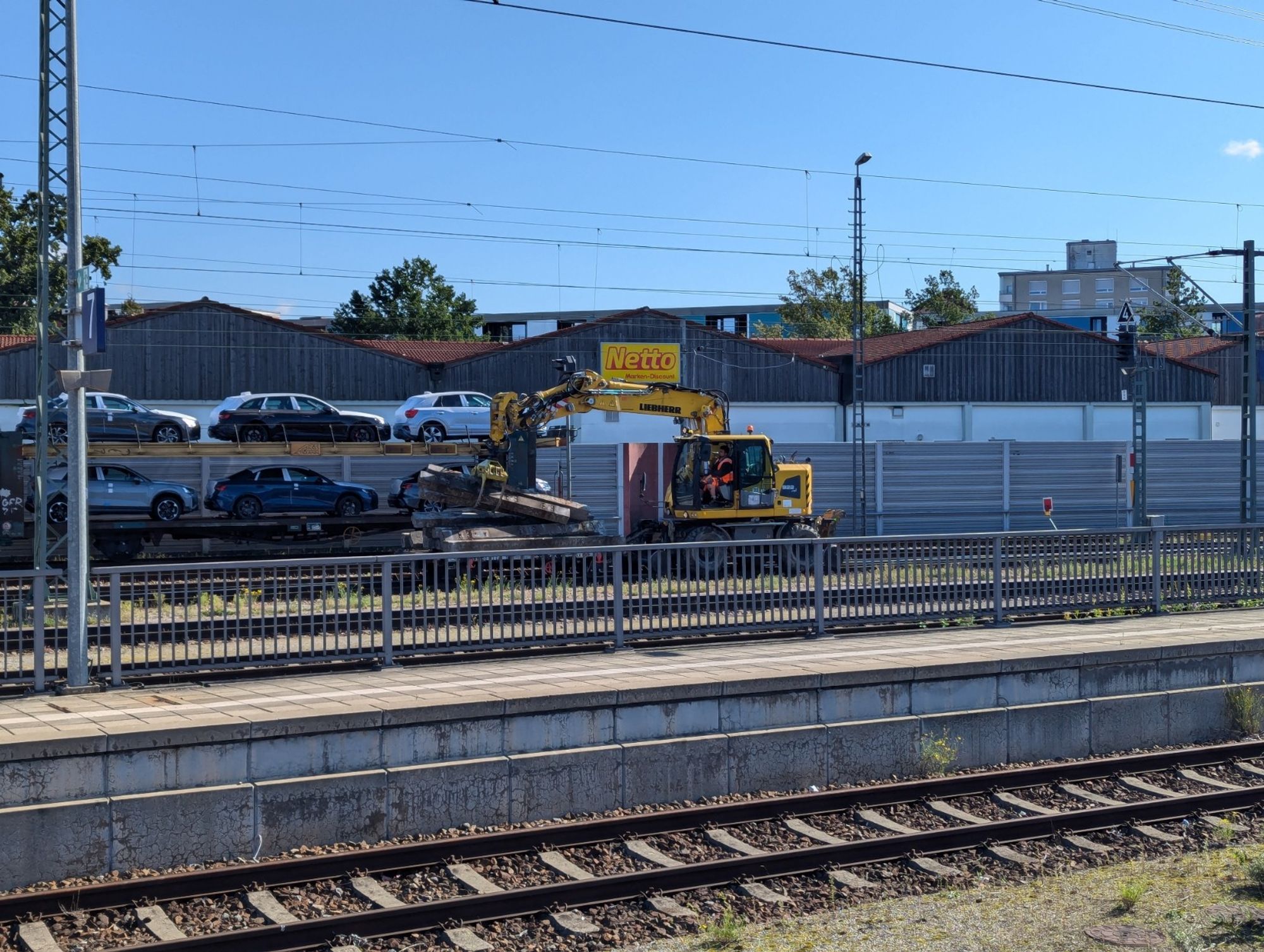 Ein Schienenbagger schiebt einen Wagen vor sich her und hält einen Haufen alter Schwellen in einer Zange