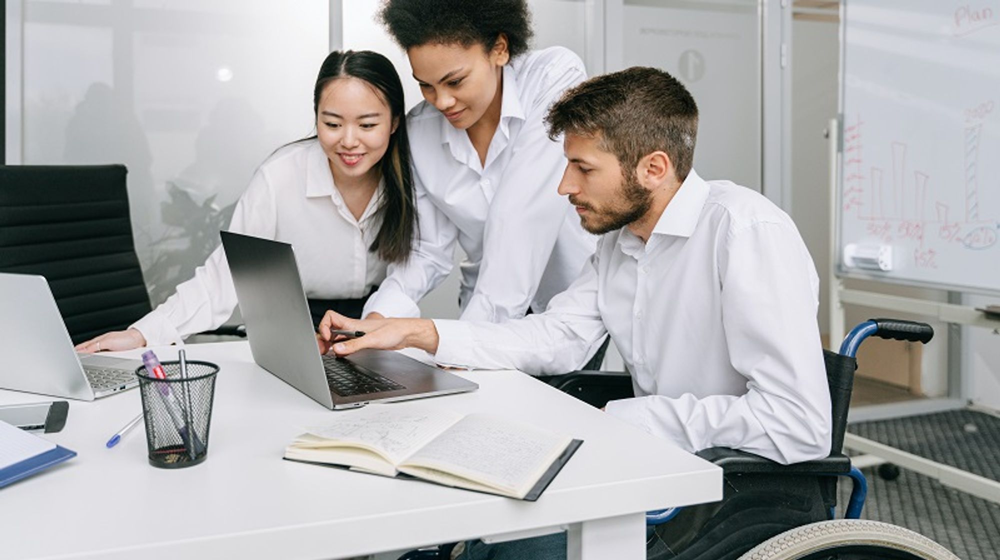 Bildbeschreibung: Ein Mann im Rollstuhl der am Laptop arbeitet in einem Büro.