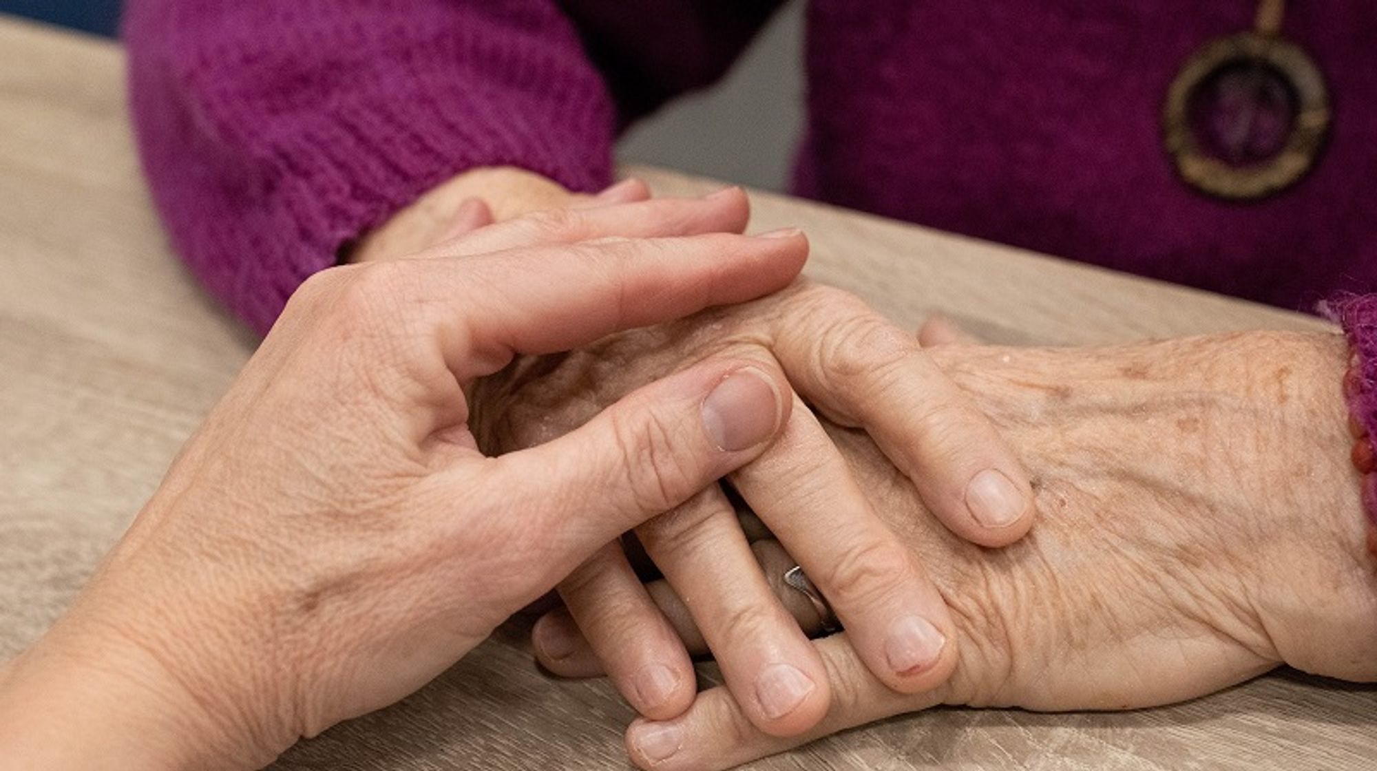 Bildbeschreibung: Eine Frau die einer anderen älteren Frau die Hände hält.