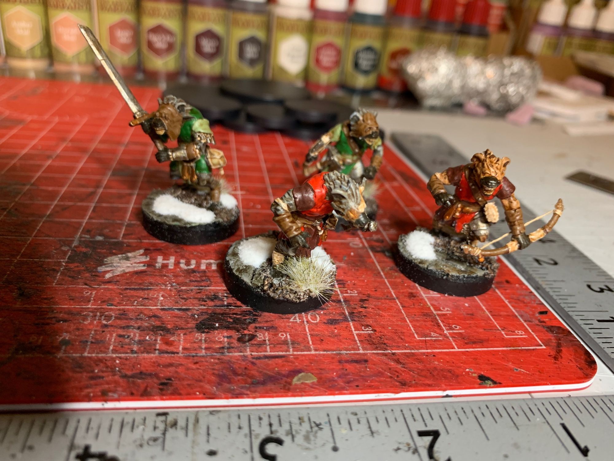 A set of four Frostgrave Gnoll miniatures, they are like a werewolf but a hyena-man instead of a wolf man. Two have green tunics and two have red tunics, they have a variety of weapons.