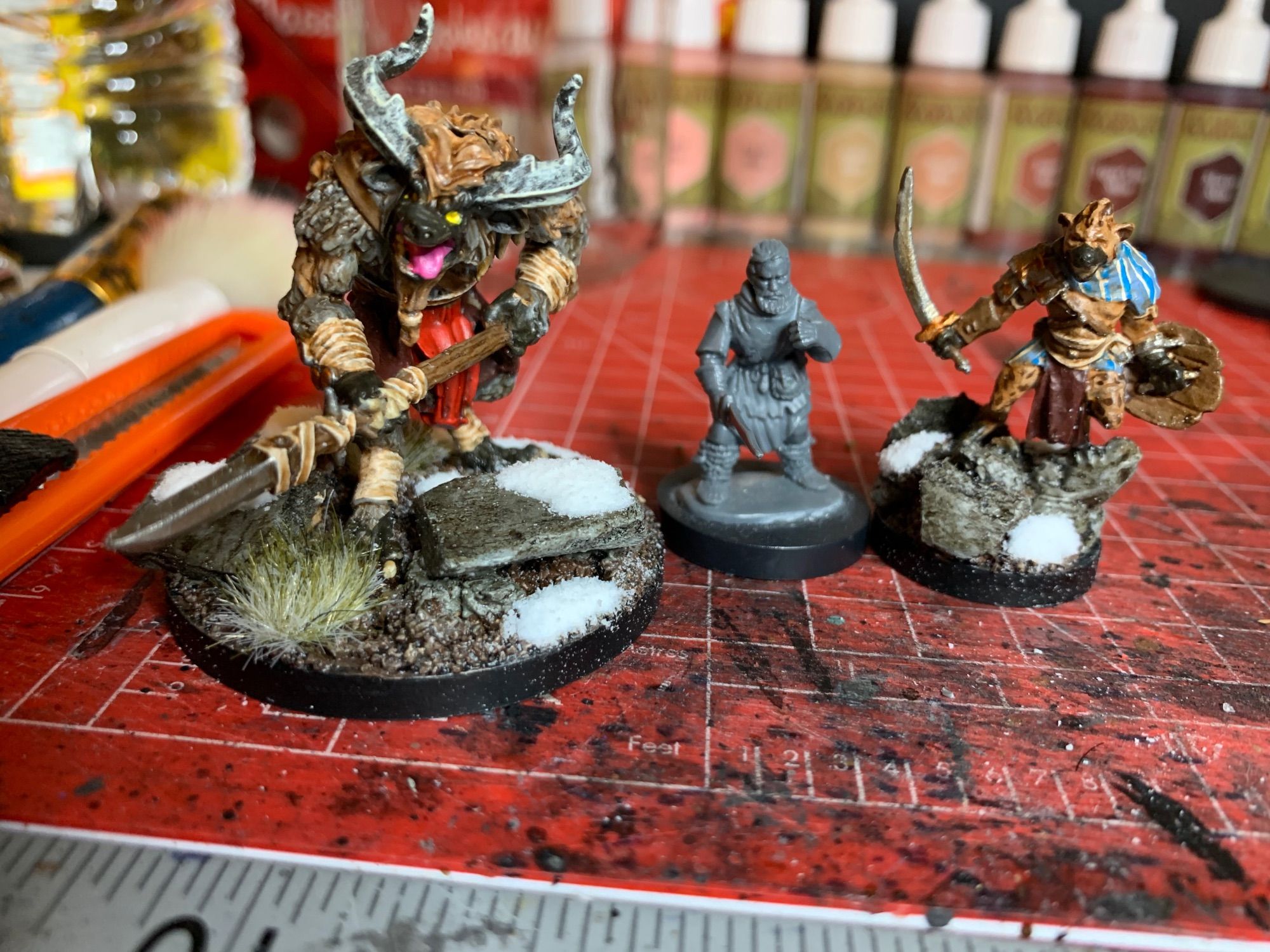 In this picture there are three miniatures, the middle is an unpainted Frostgrave human. The one on the left is a Borock, which is a large Minotaur/Gnoll hybrid that’s standing with its spear. The right mini is a a Gnoll warchief, which is just a normal Gnoll, a hyena-man, standing on rocks dramatically.