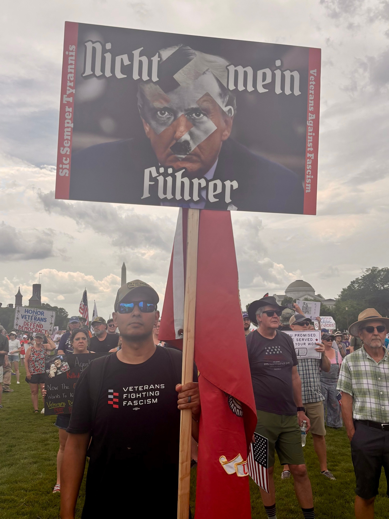 Sign held by man holding a Marine flag.  Sign says Nicht main fuhrer. 