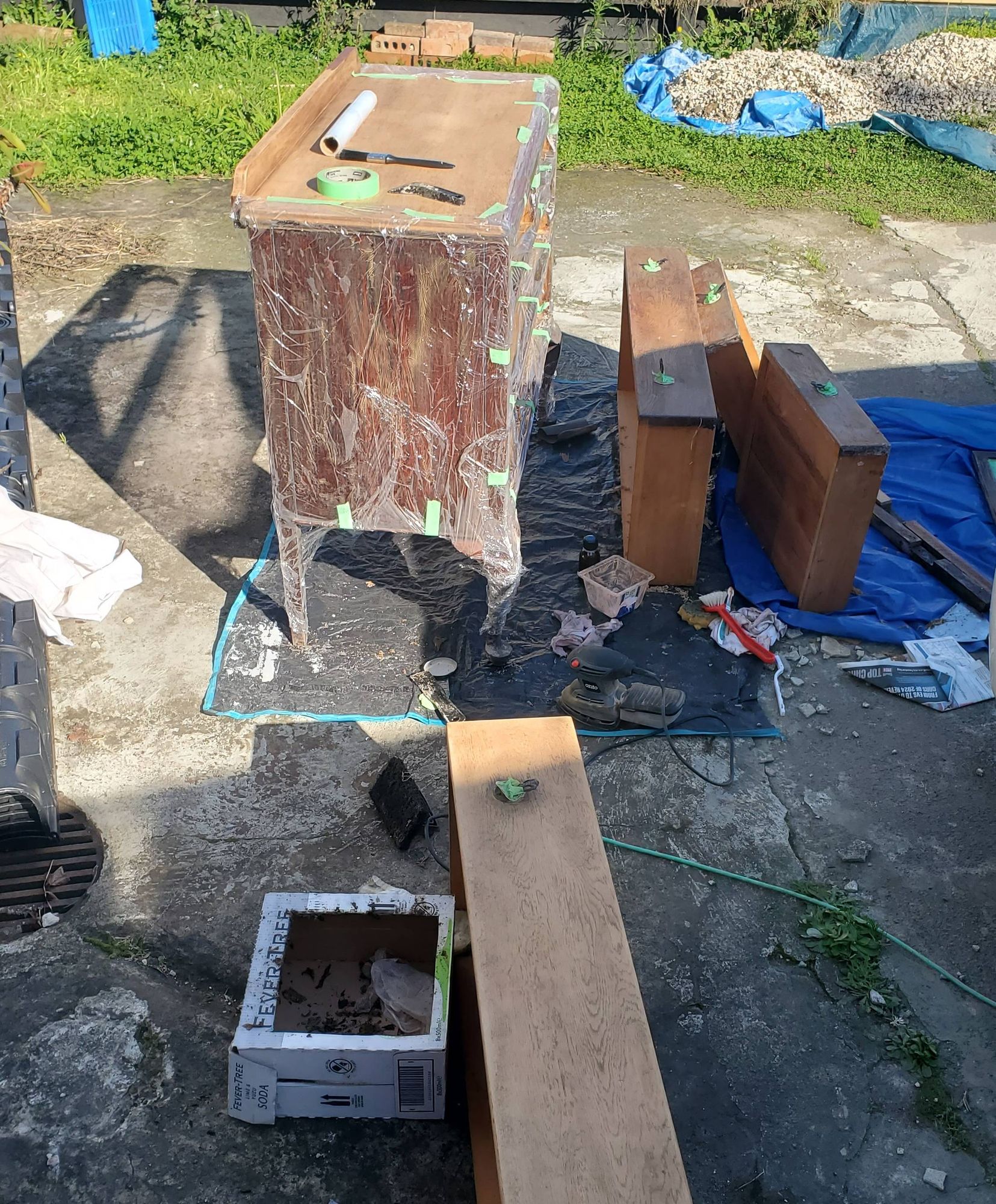 A dressing table disassembled in a driveway and being stripped of old varnish.