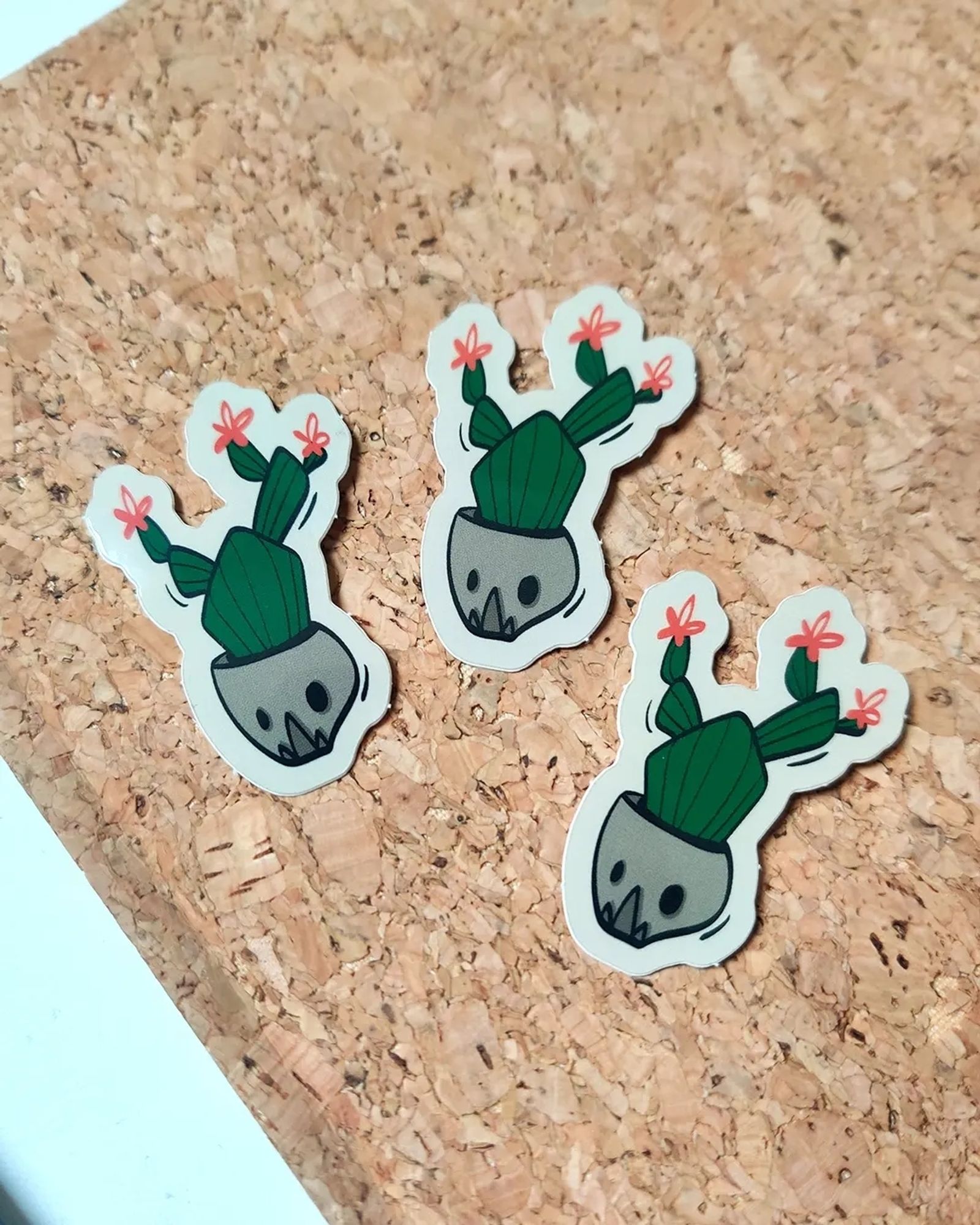 Photos de stickers colorés représentant un cactus dans un pot en forme de crâne, il y a des petites fleurs rouges a chaque extrémités du cactus.