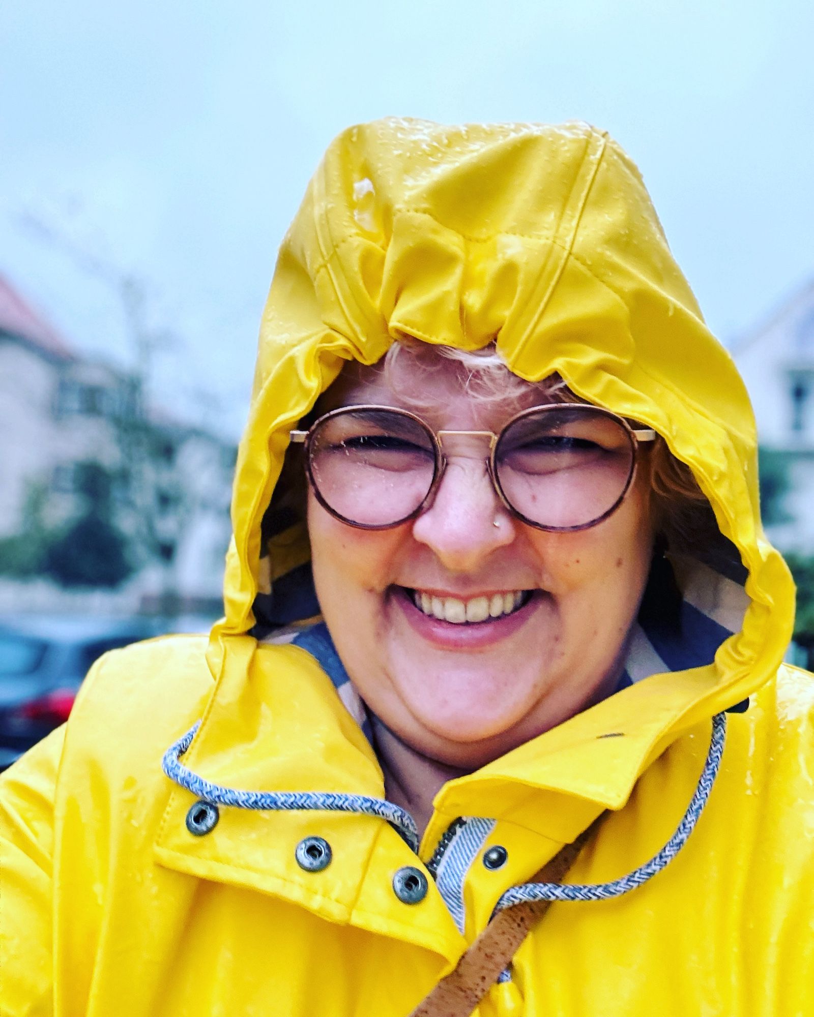 Selfie von Becci im gelben Regenparka/Friesennerz. Sie hat die Kapuze auf und kneift wegen Regen die Augen zusammen