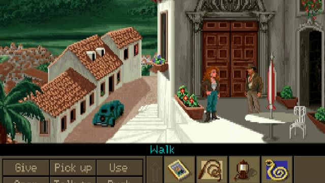 A screenshot from the game Indiana Jones and the Fate of Atlantis. A red haired female is chatting with Indy outside of a large wooden door. The graphic style is pixel.