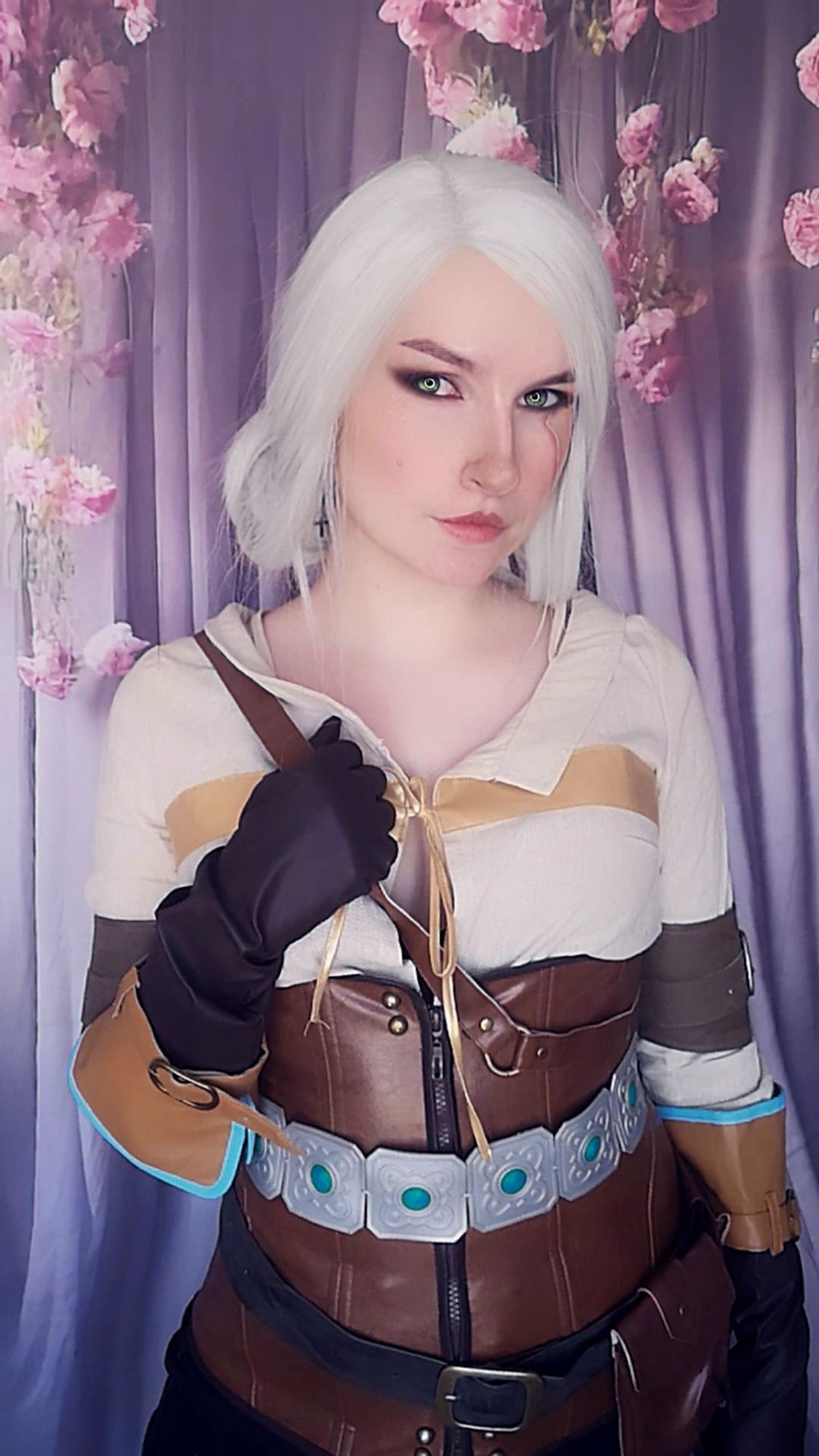 Darlazaurus en cosplay de Ciri of Cintra du jeu The Witcher, sur un fond drapé violet et rose avec des fleurs roses