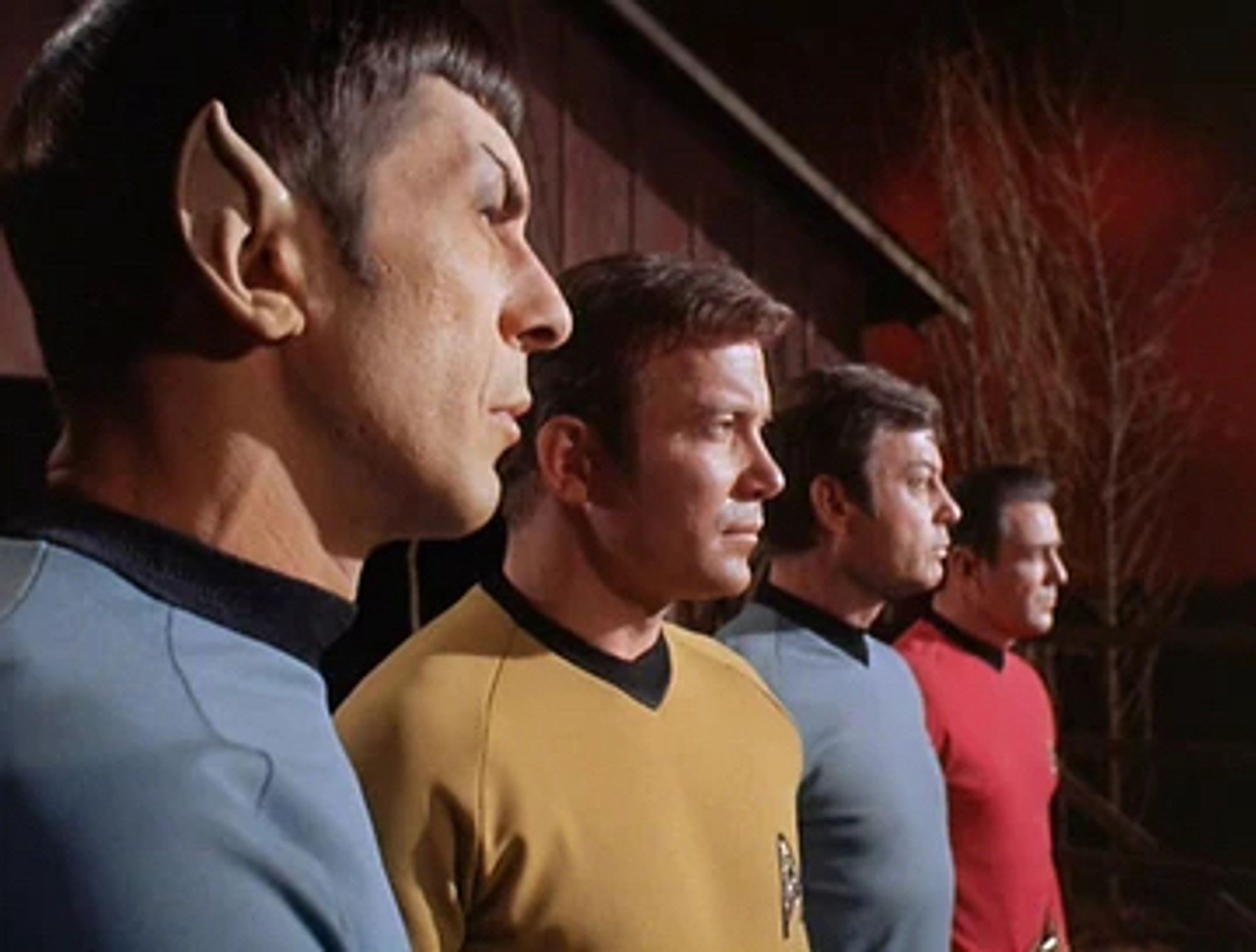 Spock, Kirk, McCoy and Scotty all standing in a line, facing right.