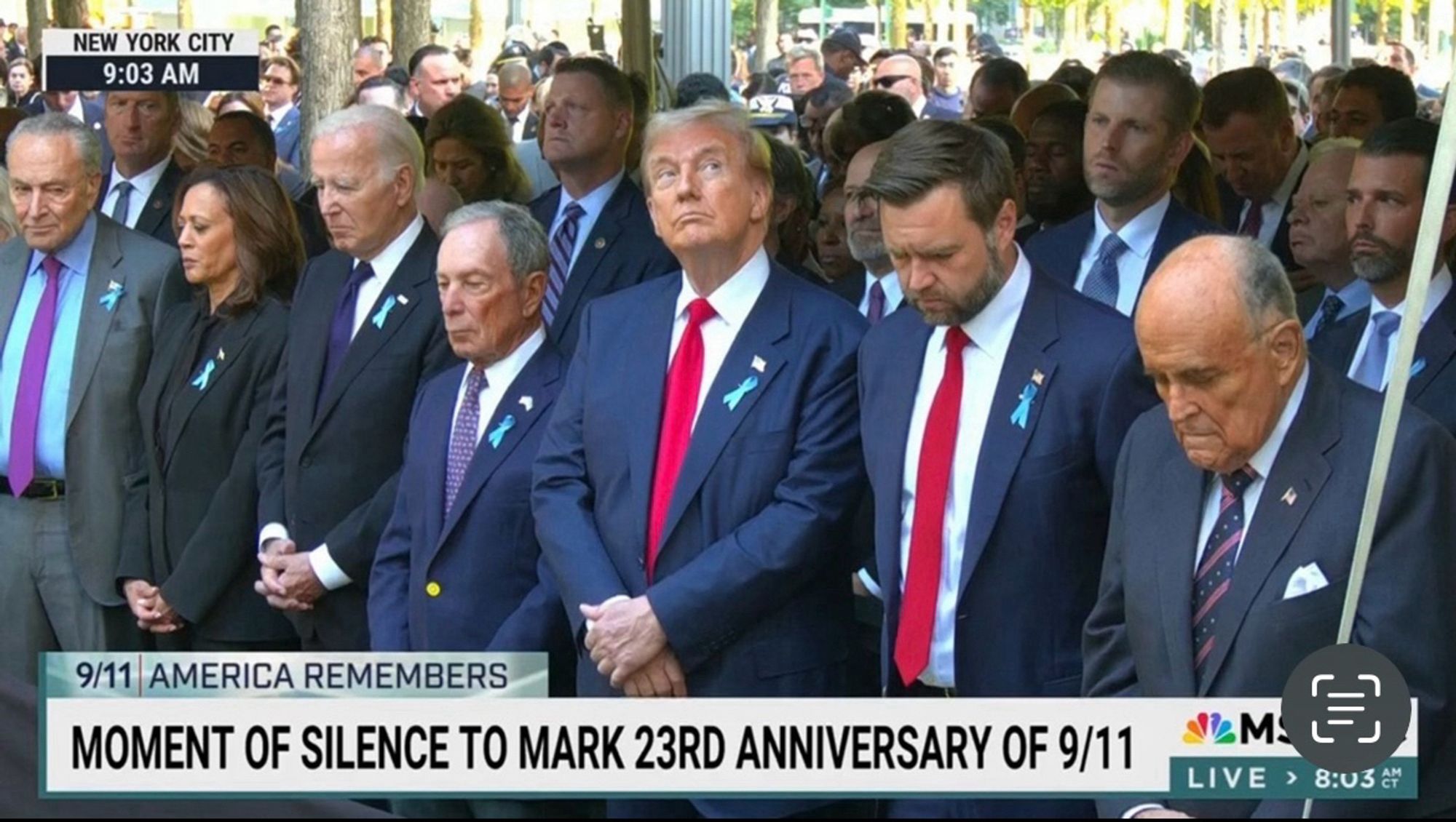 Photo of politicians during moment of silence for 9/11 victims. Schumer, Harris, Biden, Bloomberg, Vance, & Guliani looking down with solemn expressions. Trump looking up and away with an expression of disinterest.