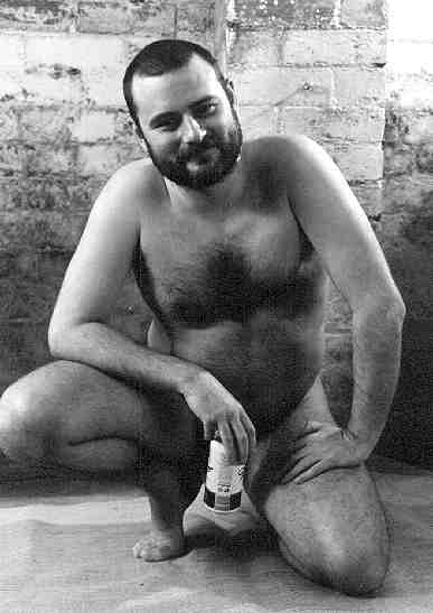 B&W photo, Naked bearded man crouching down, holding a beer can to protect his modesty