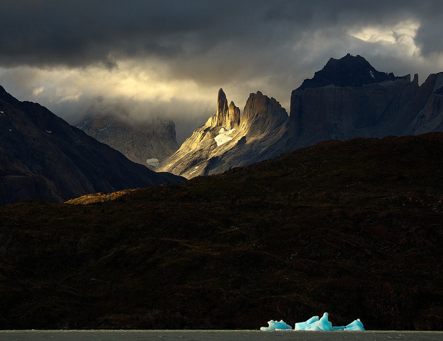 Patagonia is breathtaking, the ever changing light & weather is what makes it so very special. In Torres del Paine National Park, a spot lit iceberg is dwarfed by mountains already in the shade, except for the jagged summit, bathed in the warm afternoon sun.