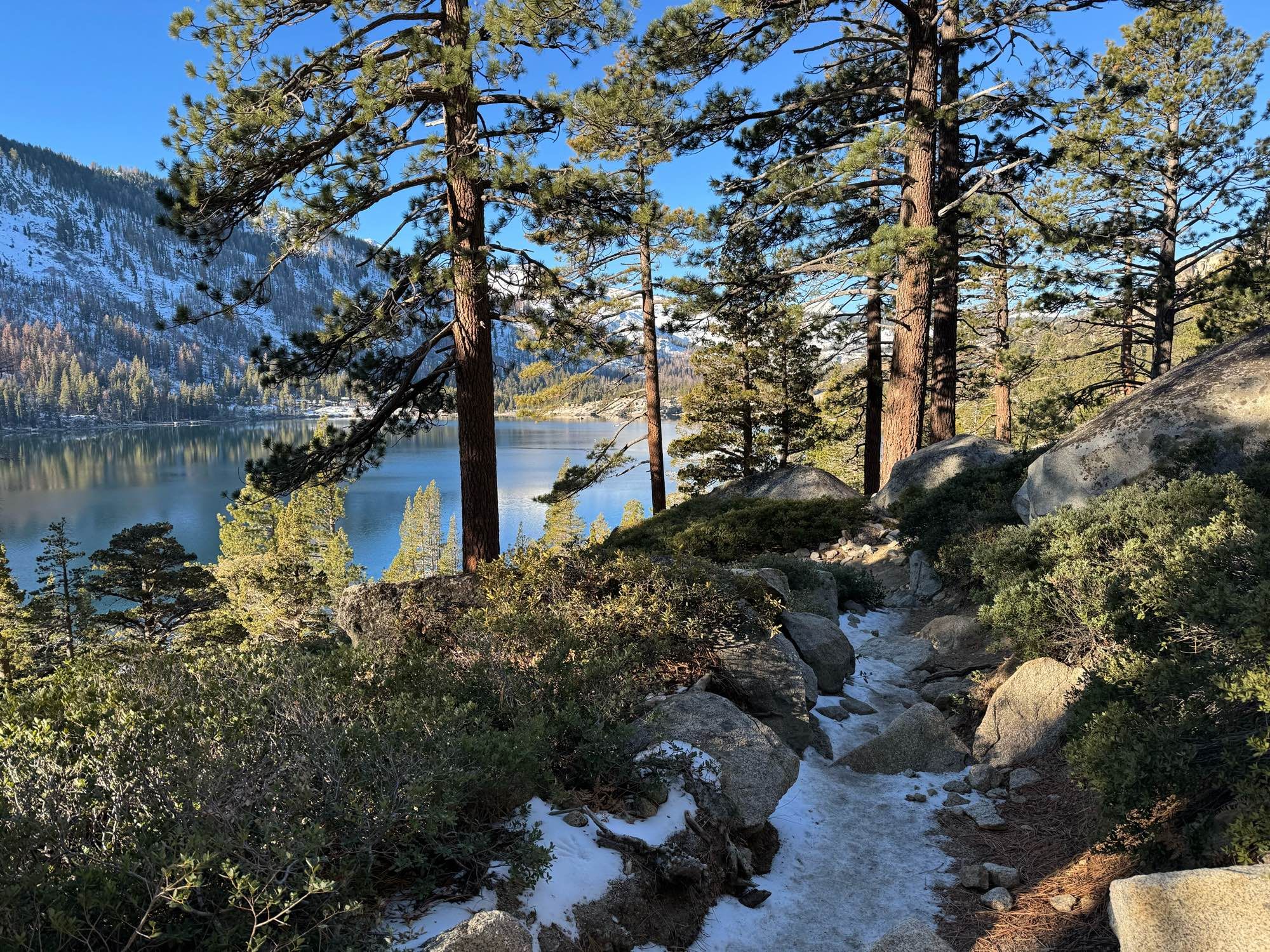 Iced over trail alongside Echo Lake, with snowy mountains in the background and trees on a side of the trail