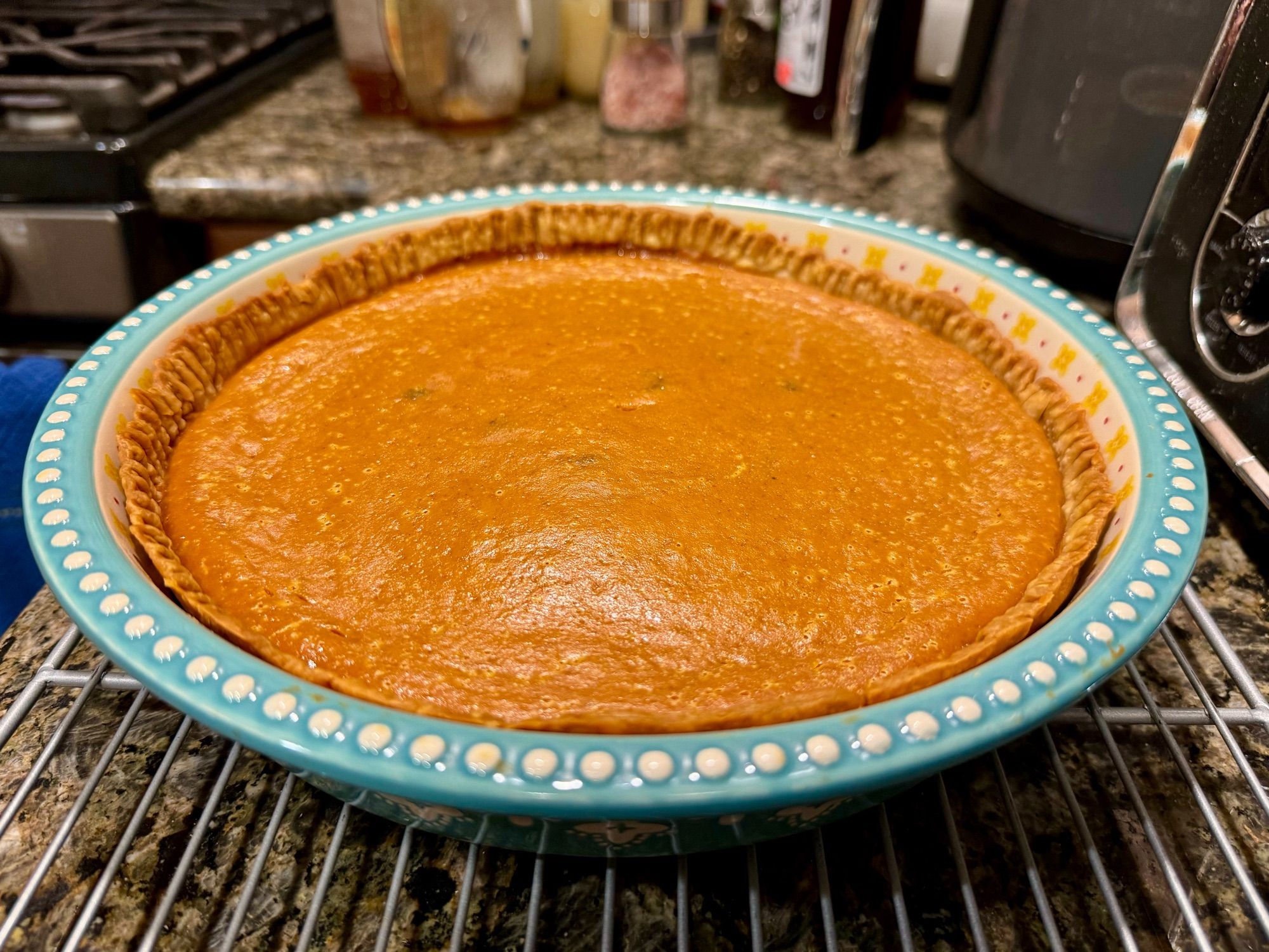 Pumpkin pie in a blue ceramic baking dish, cooling on a rack.