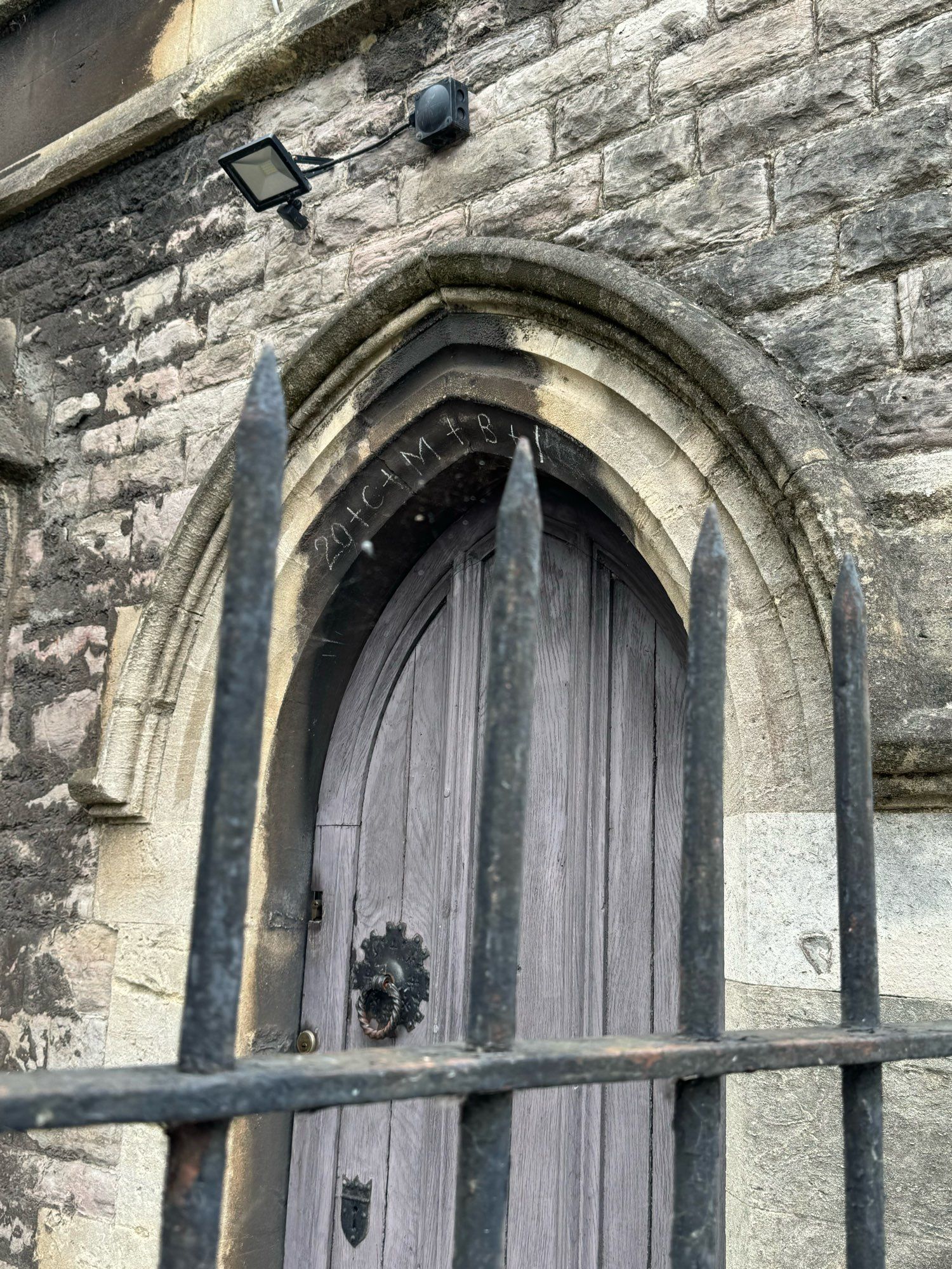 Gothic door war with blessing in arch behind iron railings