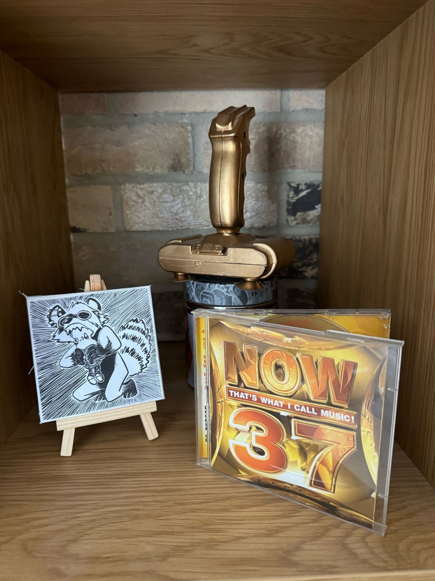 A copy of Now That’s What I Call Music! 37, which takes pride of place next to a gold spray painted controller and a drawing of me eating a minion