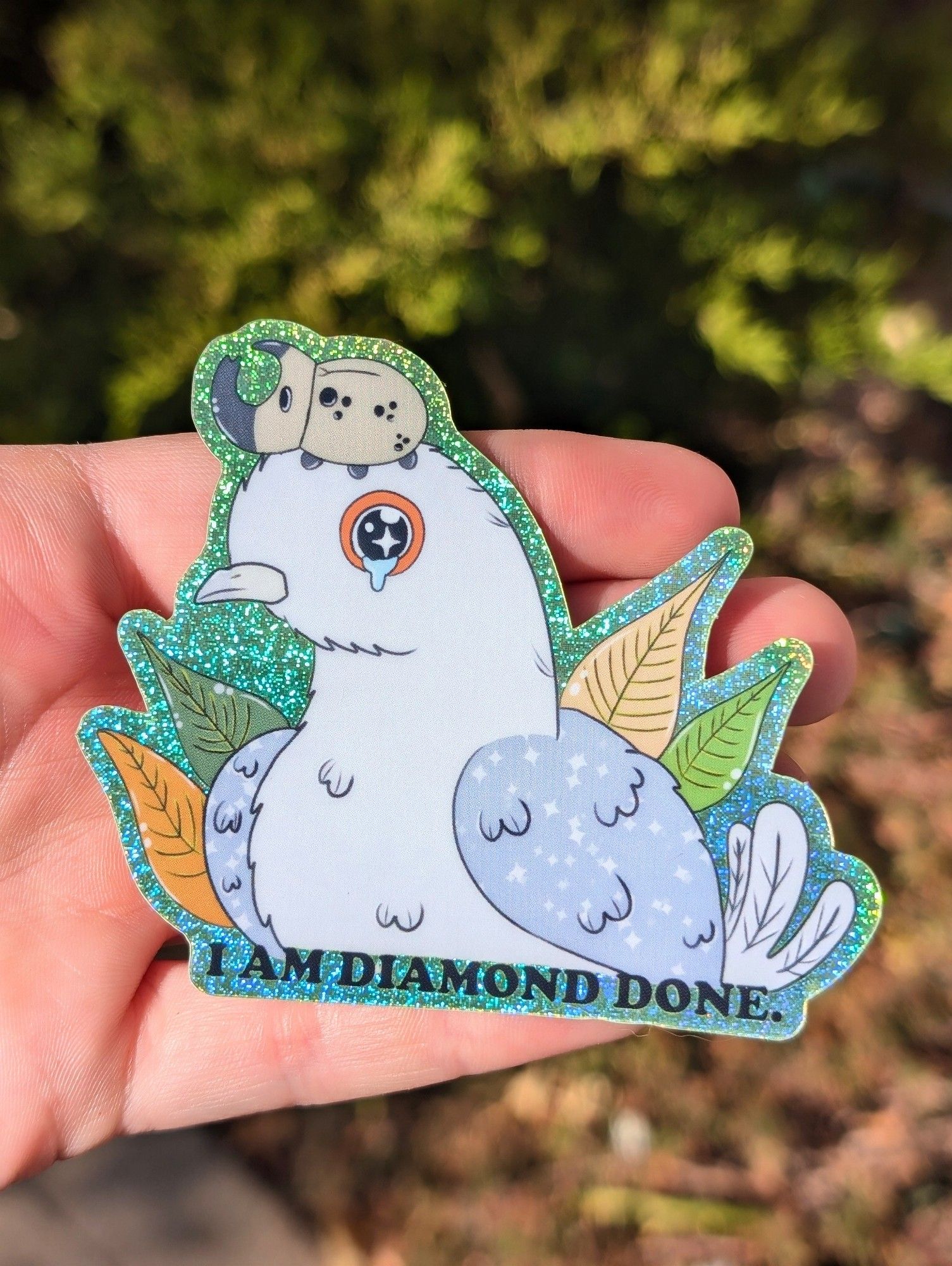 Glittery sticker featuring a crying Diamond Dove with a Rhino Beetle on its head and the words "I am Diamond Done."