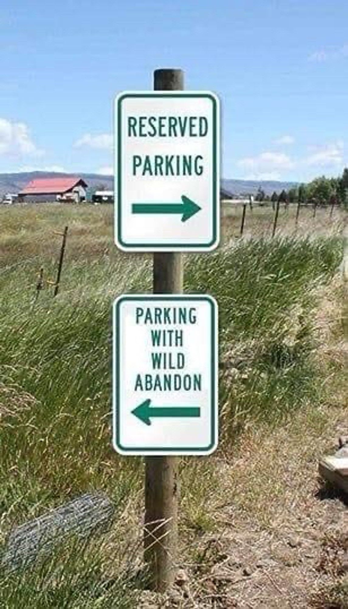 Two white signs with green writing on them mounted one above the other on a wooden post. 
The top one says Reserved Parking. 
The bottom one says Parking With Wild Abandon.